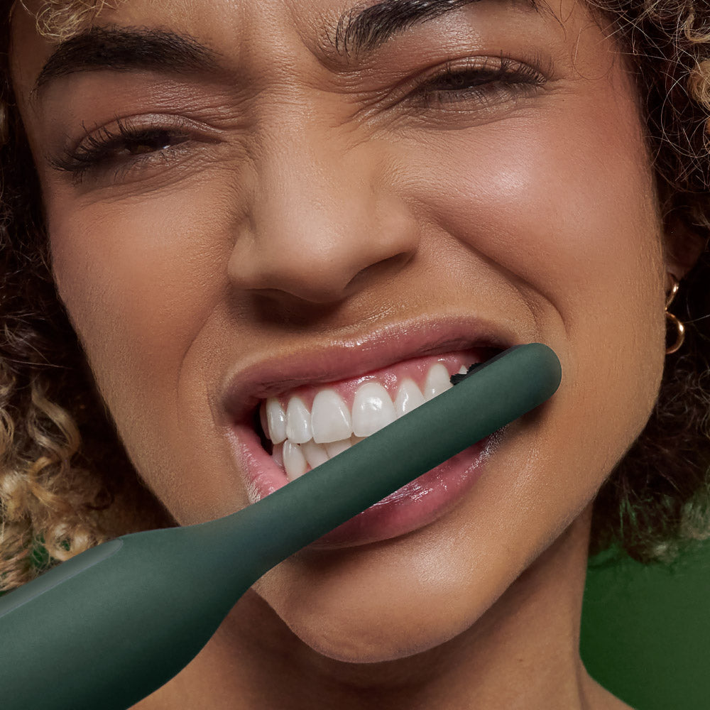 Close-up of a woman holding a green toothbrush to her mouth