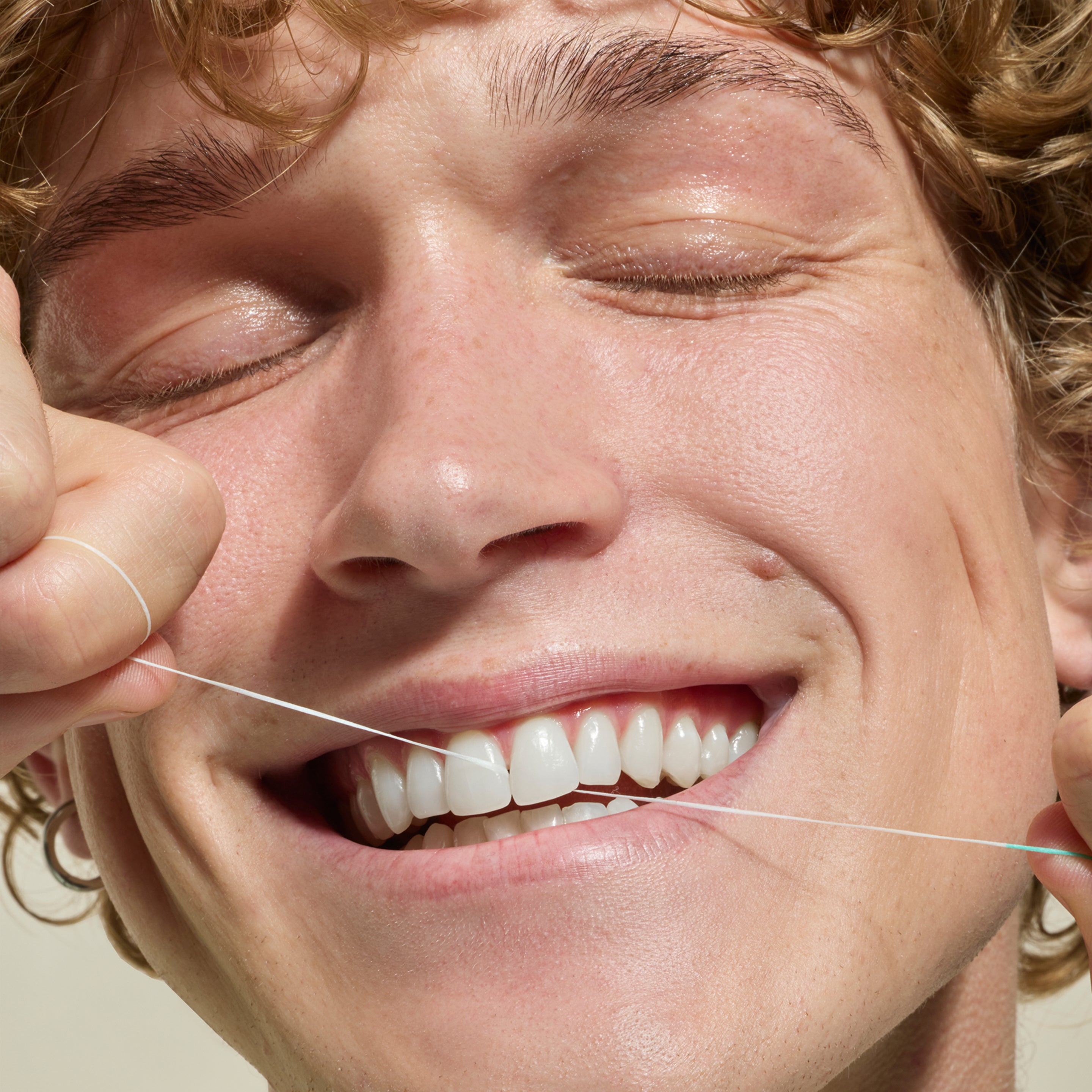 Person using dental floss with a neutral background