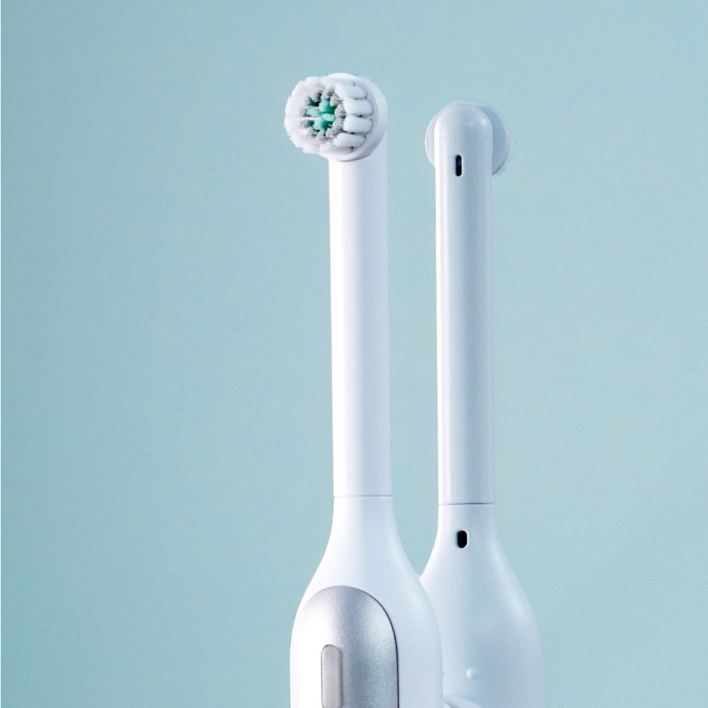 White quip Rev oscillating electric toothbrush standing in front of a mirror, reflecting the back of the toothbrush head and handle.