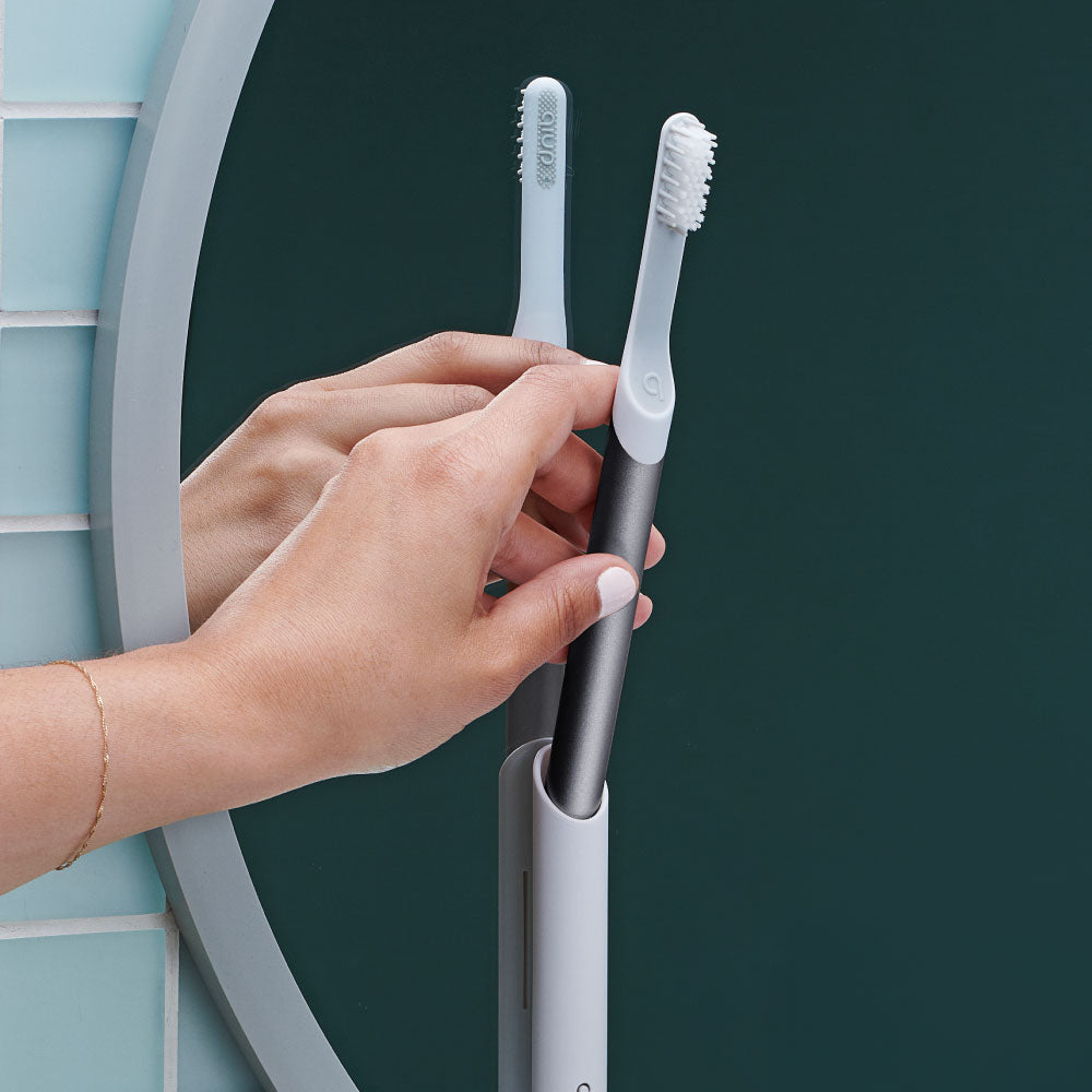 Hand holding Sonic toothbrush with a mirror in the background showing it's reflection.