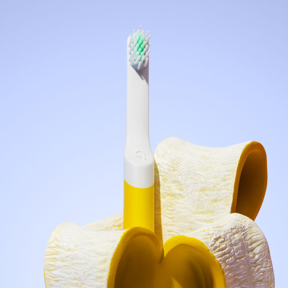 Yellow toothbrush with a white handle and green bristle head on a textured yellow stand against a light blue background.
