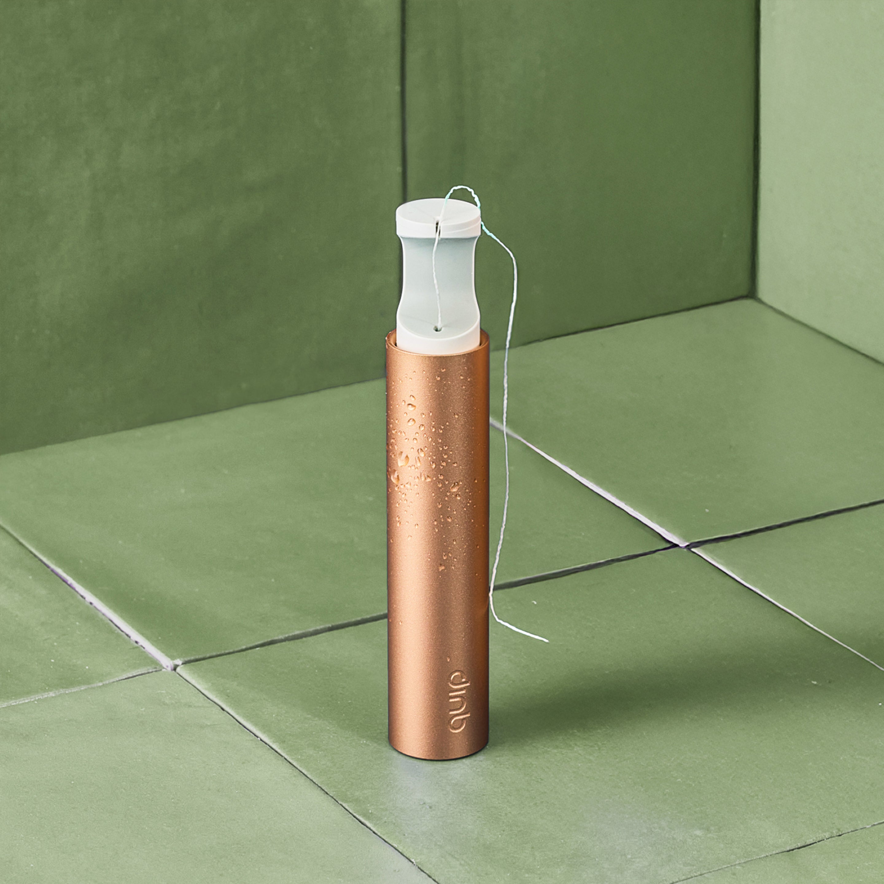 Copper-colored travel toothbrush holder with white brush on a green tiled surface
