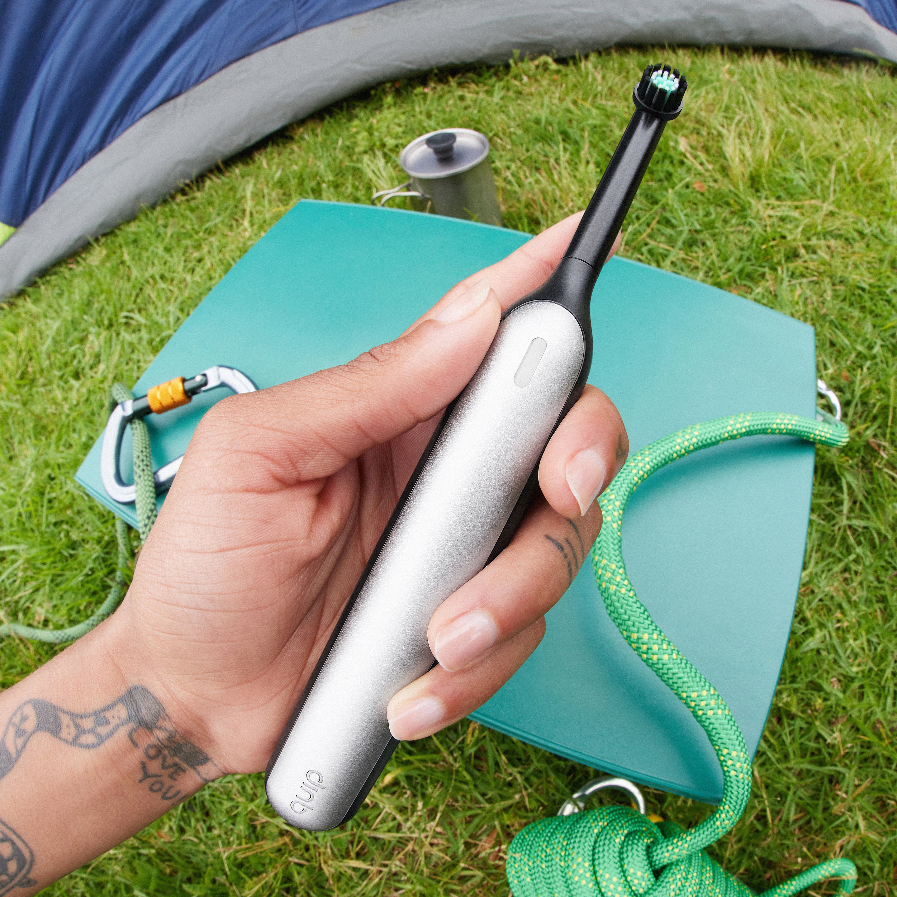 Rev Oscillating Toothbrush in Gray Shadow held outdoors beside camping gear on grass.