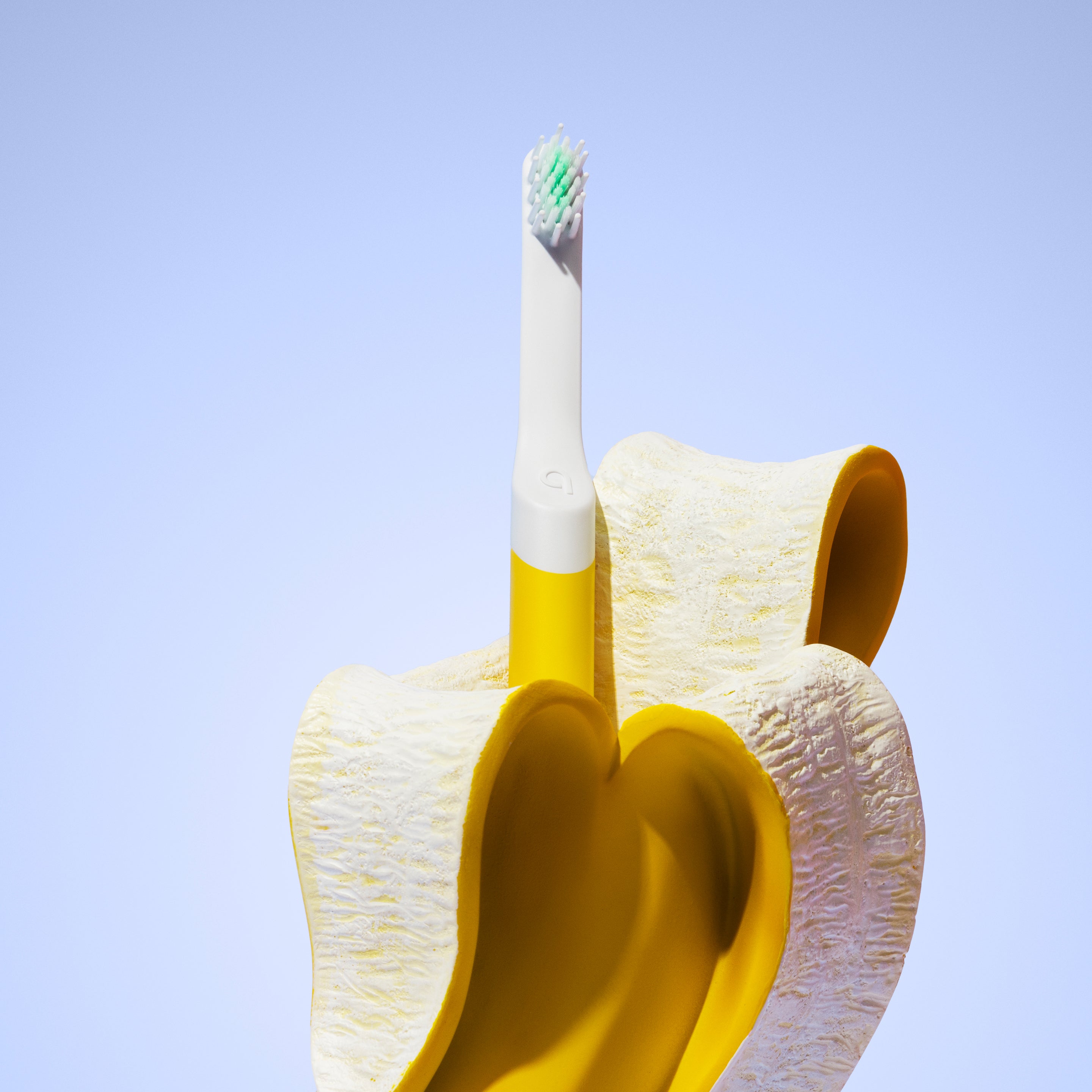 A yellow quip Kids Sonic toothbrush standing upright inside an open banana peel against a light blue background.