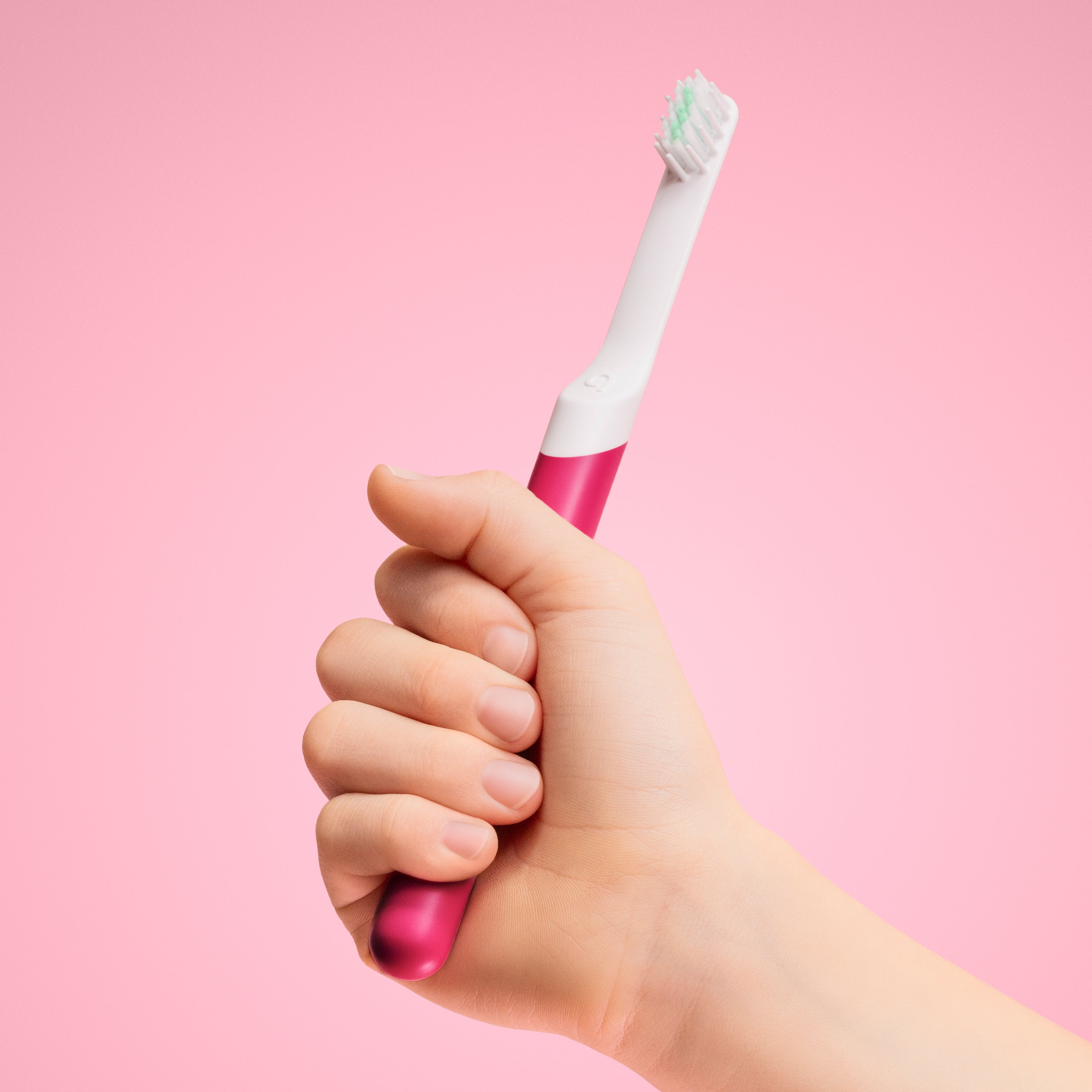 A hand holding the pink ‘Wonder’ color variant of the quip Kids Sonic toothbrush against a soft pink background.