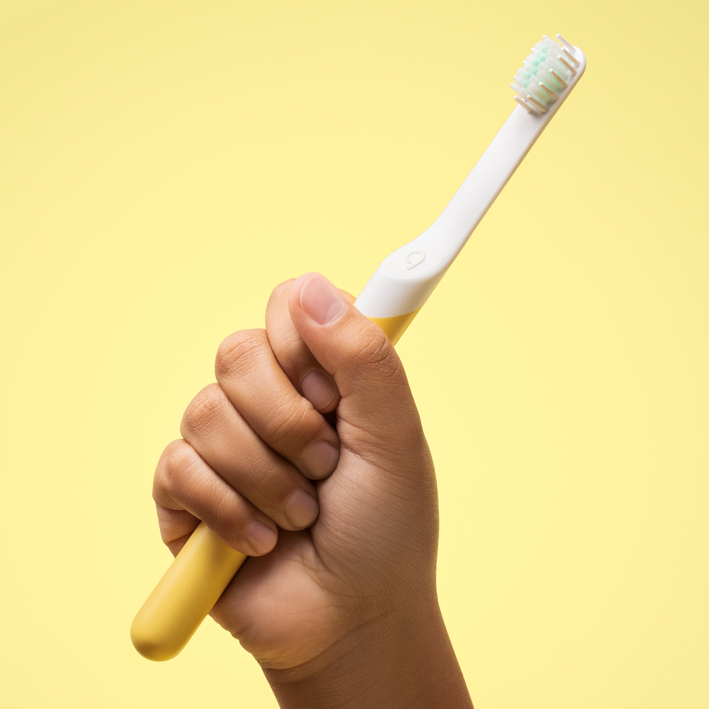 A child's hand holding a yellow and white sonic toothbrush with a blue brush head.