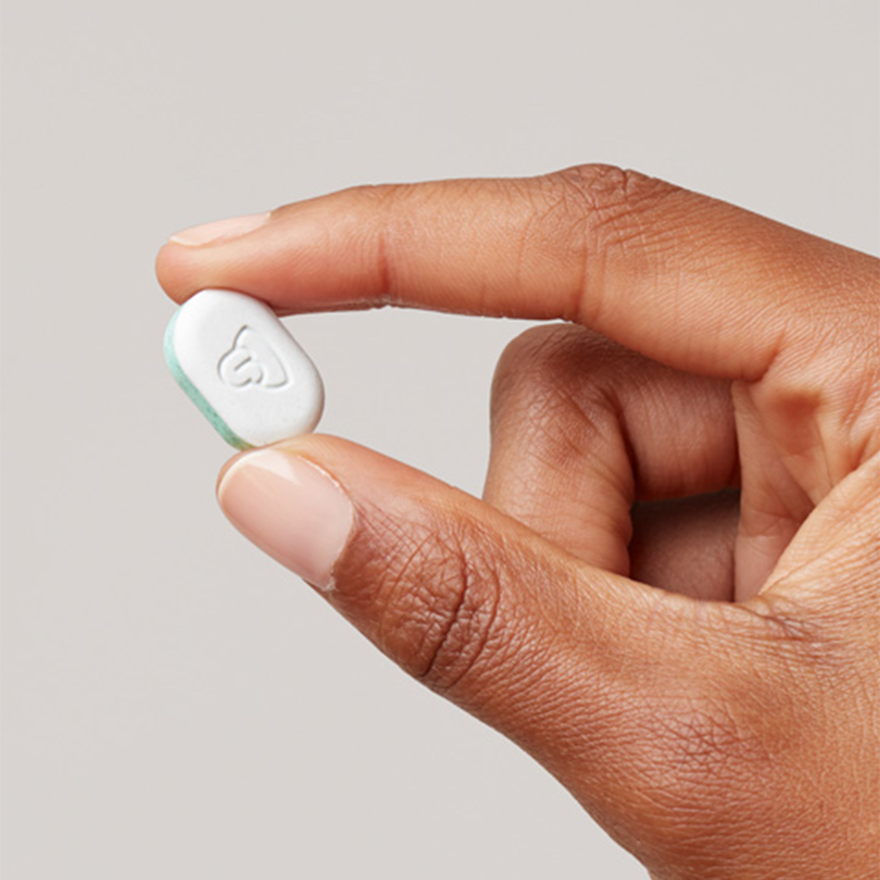 Hand holding a single white mint with a small embossed logo on a neutral background.