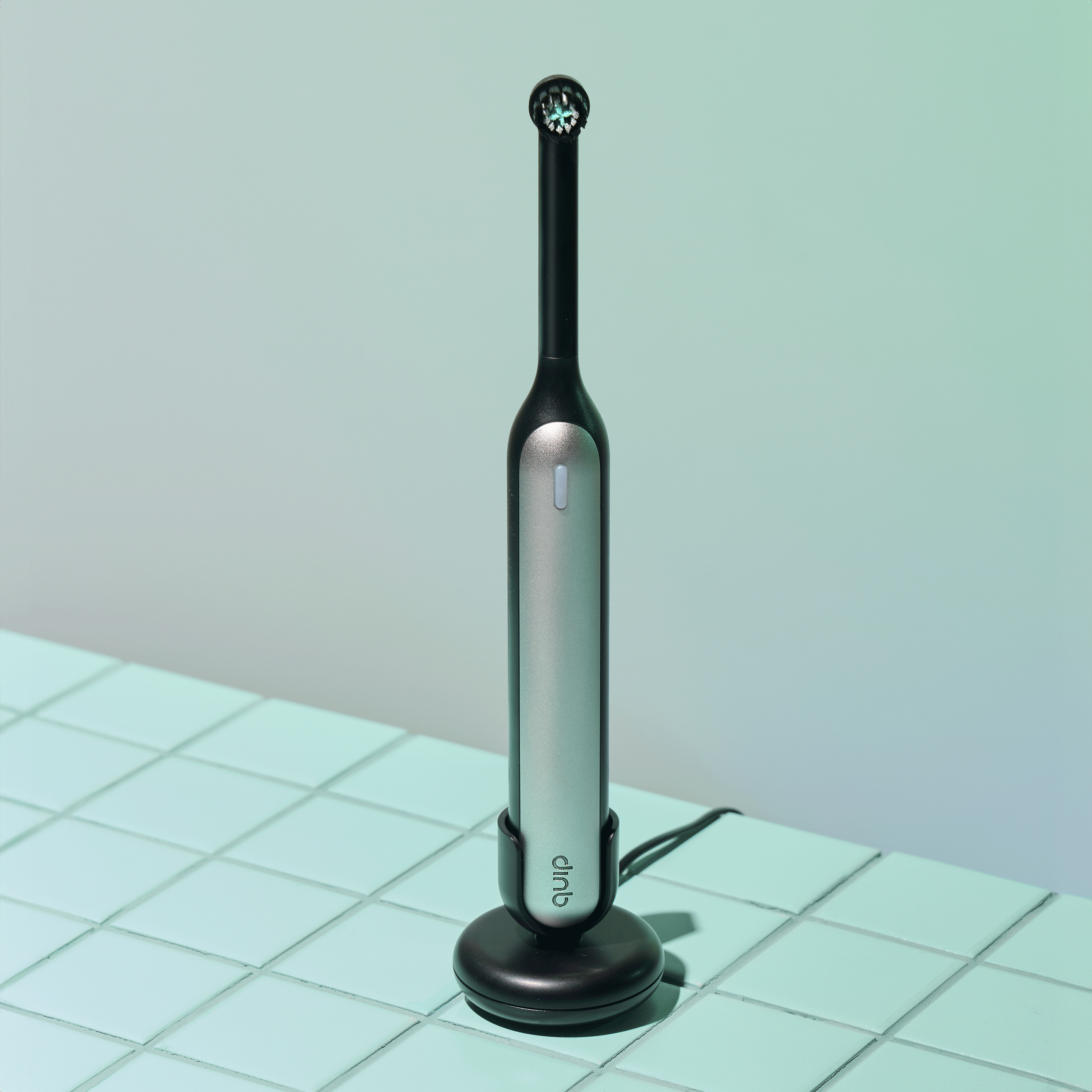 Black quip Rev Oscillating Electric Toothbrush on its magnetic charging base, shown from a front-side angle.
