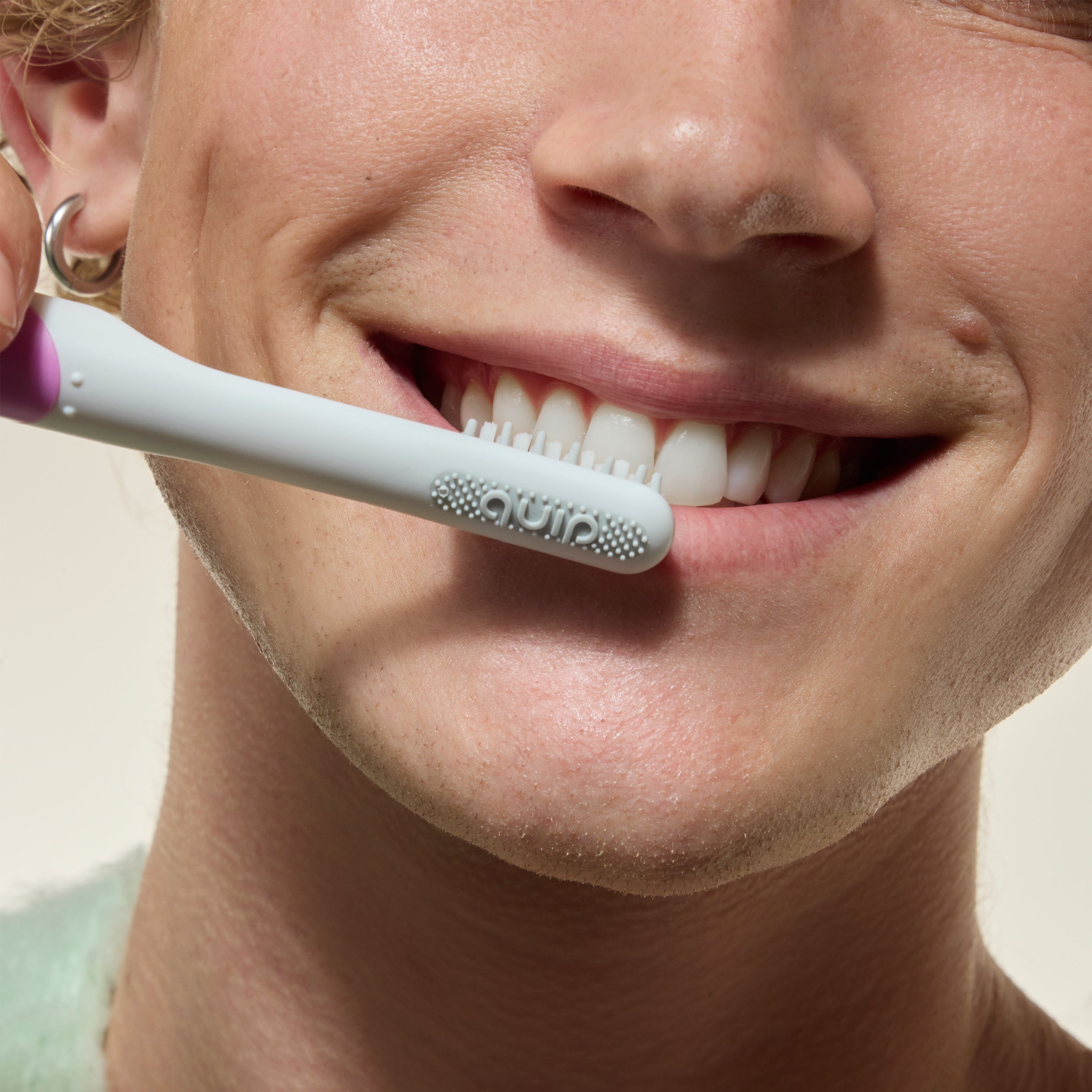 Person smiling while brushing their teeth with a white toothbrush held against their front teeth.