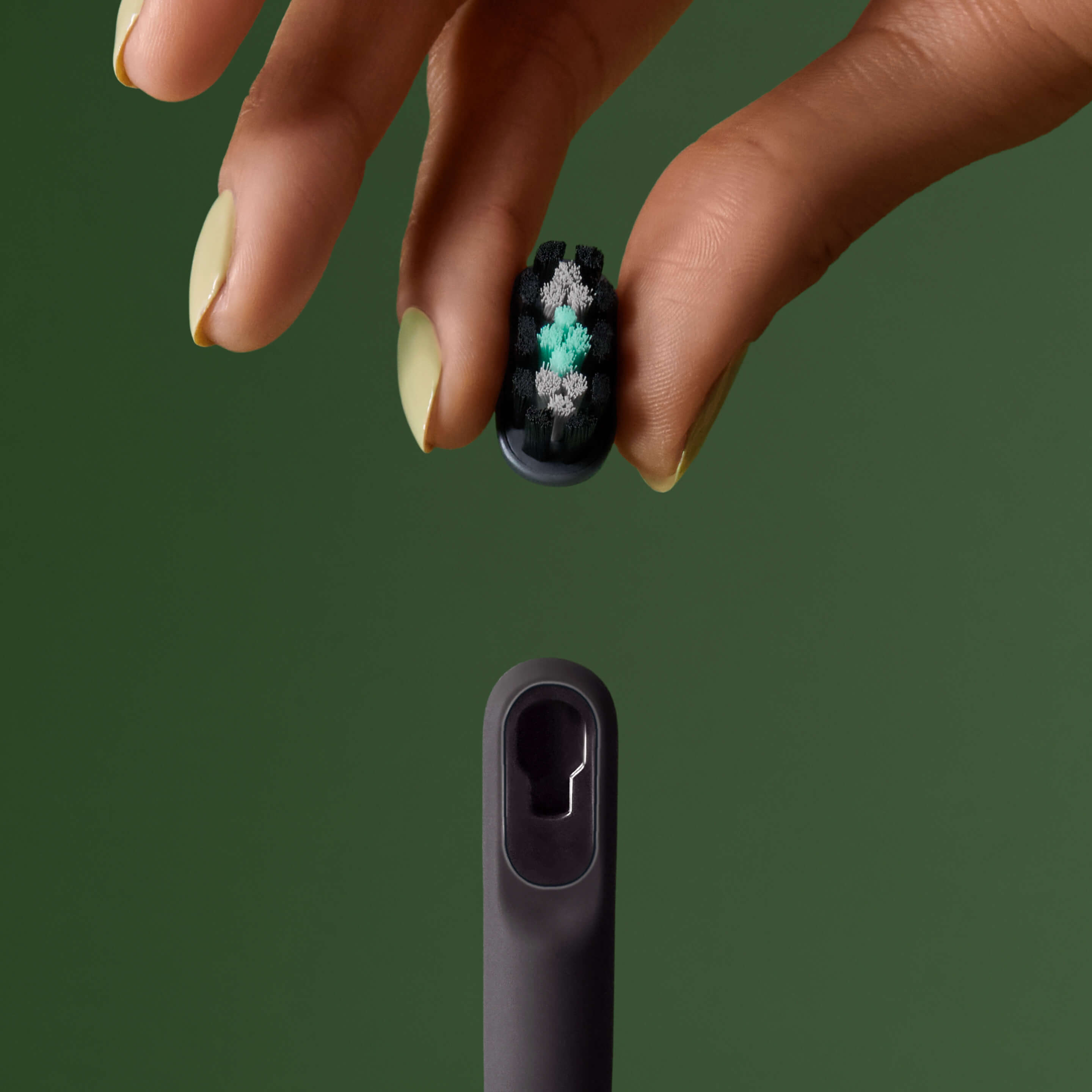 Hand holding a small brush head above a toothbrush handle, ready to attach.