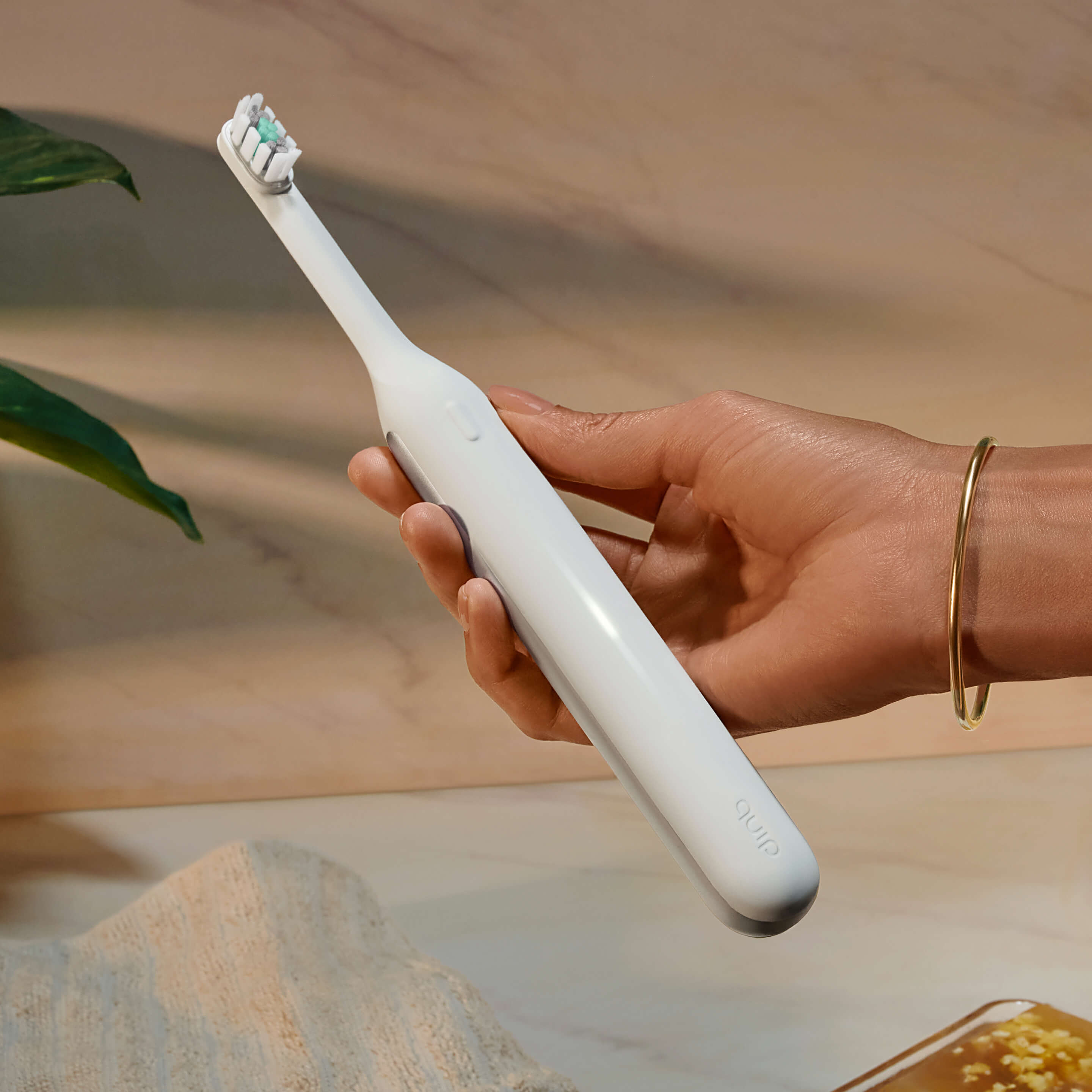Hand holding the Ultra™ Next Generation Smart Sonic Electric Toothbrush in Stone color.