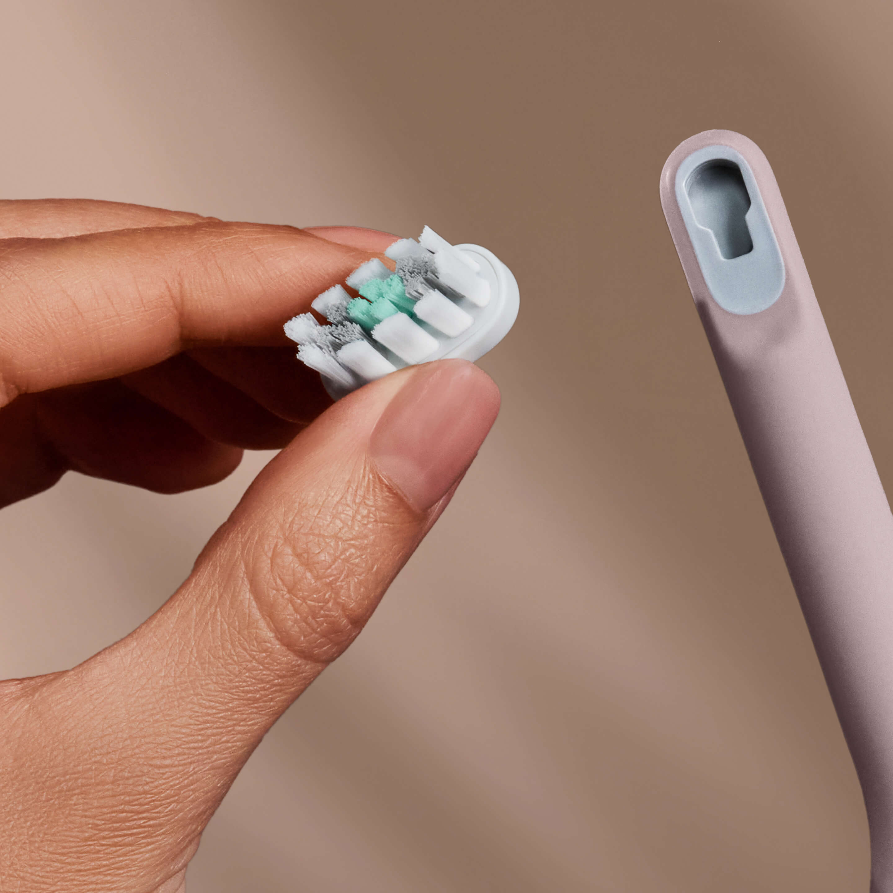 Hand holding a white brush head next to a pink toothbrush handle, ready to attach.