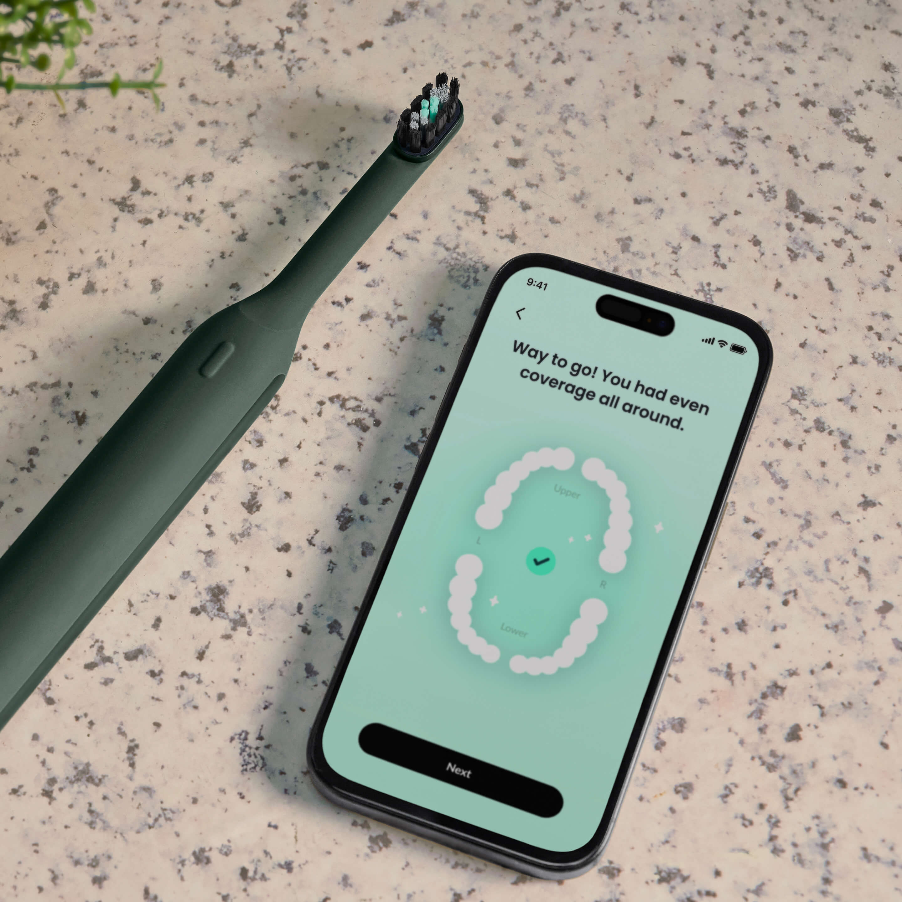 Ultra™ Next Generation Smart Sonic Electric Toothbrush in Moss color shown on a countertop next to a smartphone displaying brushing feedback in the companion app.