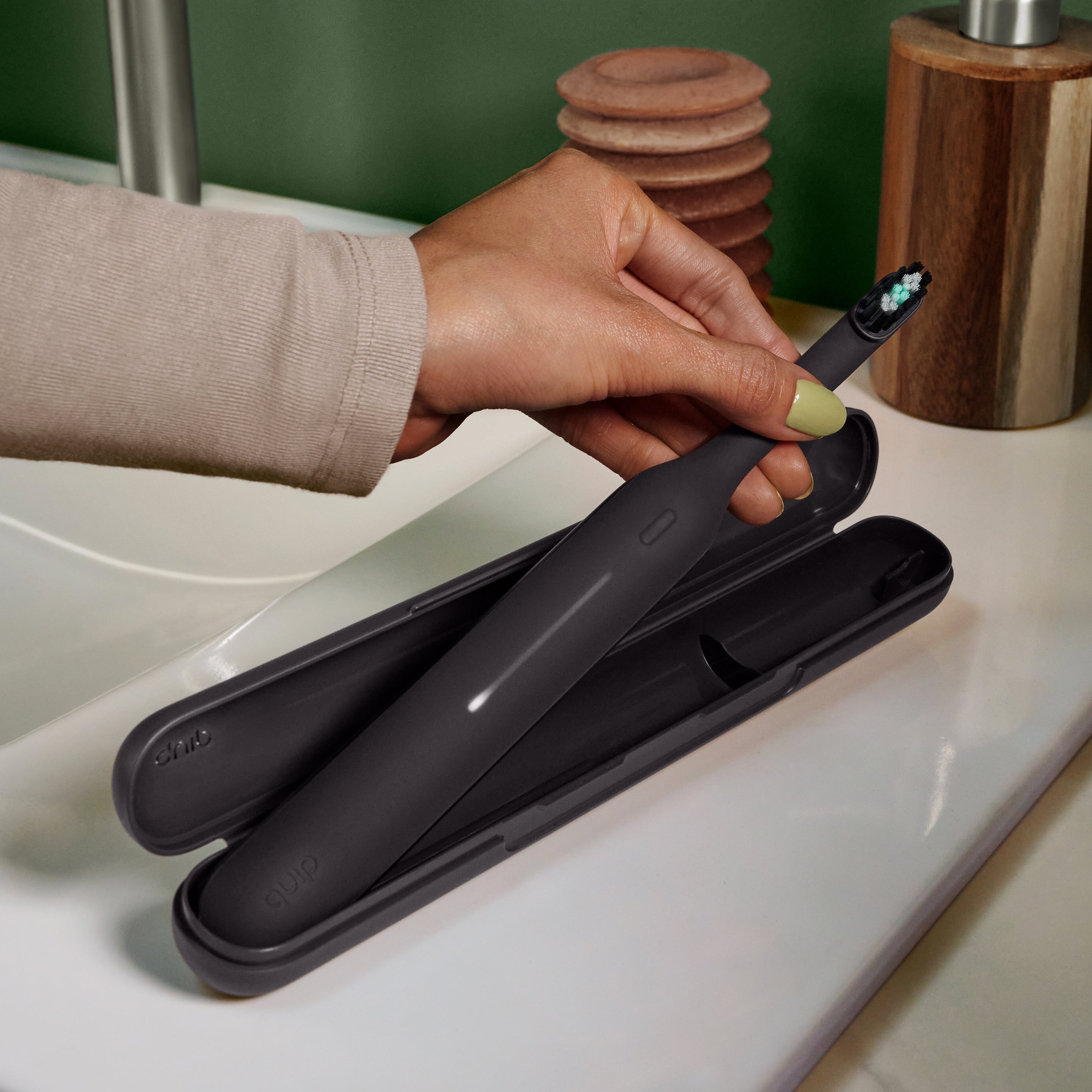 Hand placing a dark gray electric toothbrush into a matching travel case on a bathroom counter.