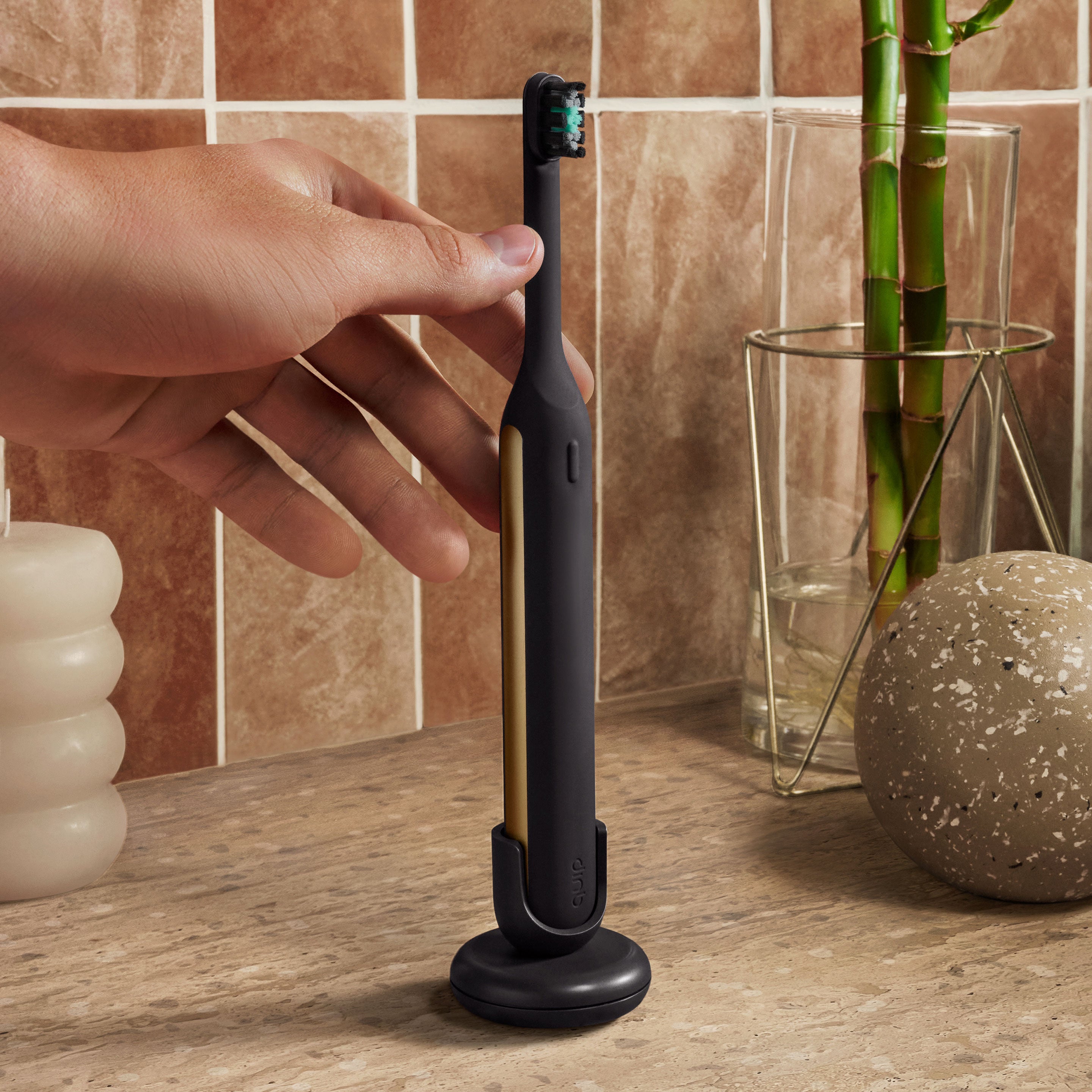Hand placing a black and gold electric toothbrush into its stand on a bathroom counter.