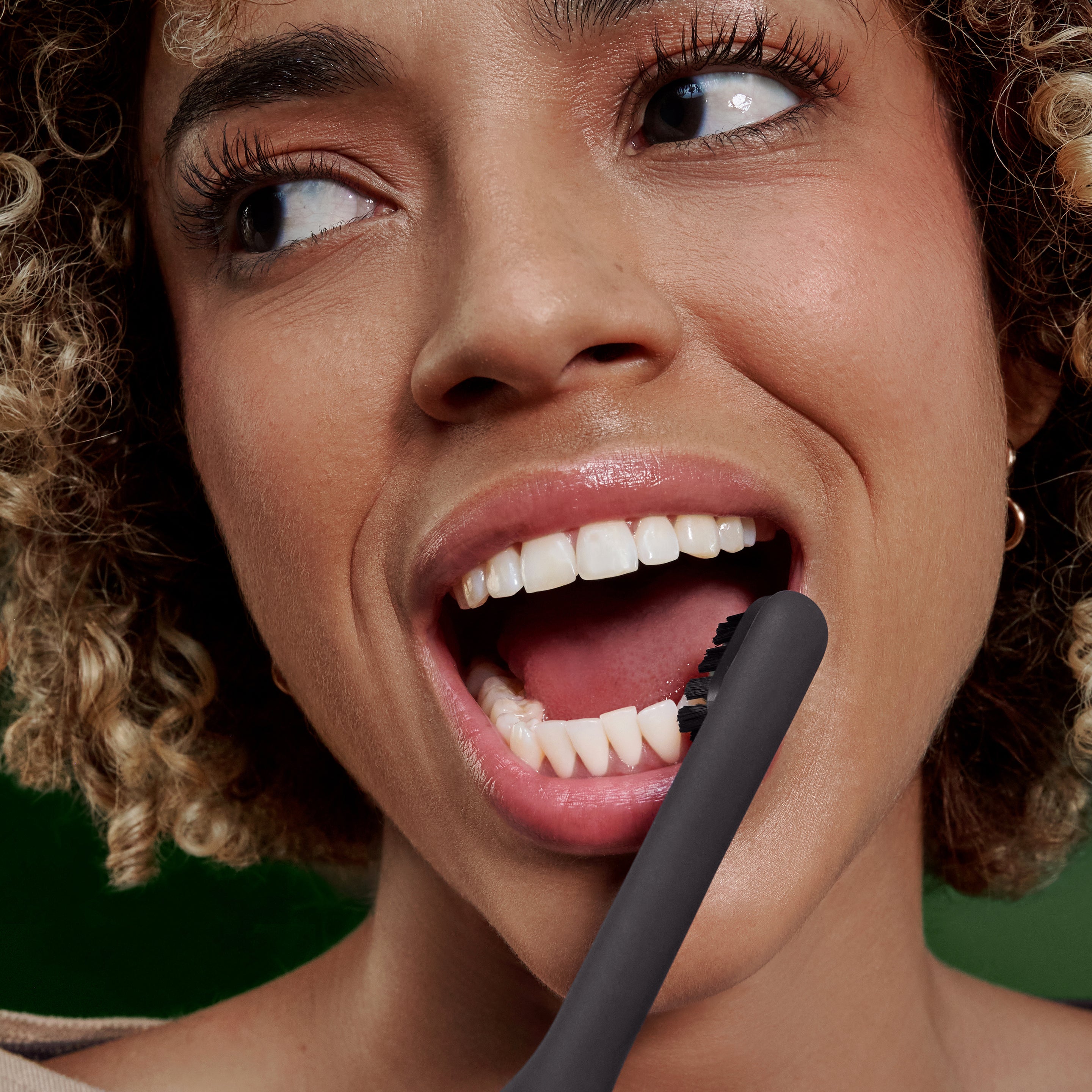 Person brushing teeth with the Ultra™ Next Generation Smart Sonic Electric Toothbrush in Onyx color, shown in close-up while smiling.