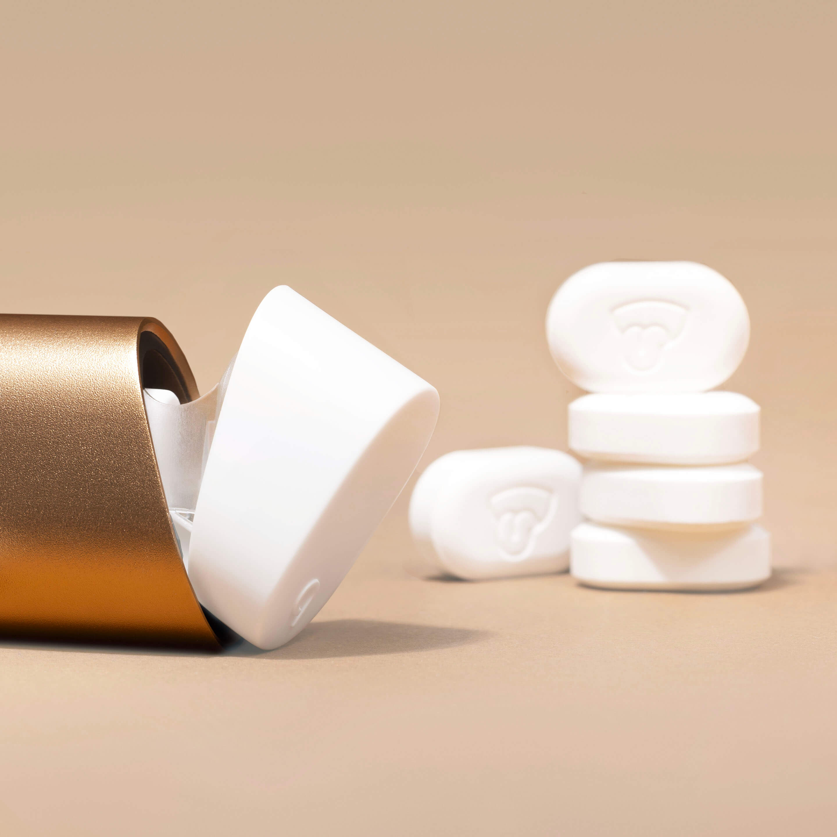 White wireless earbuds with a gold charging case on a beige background