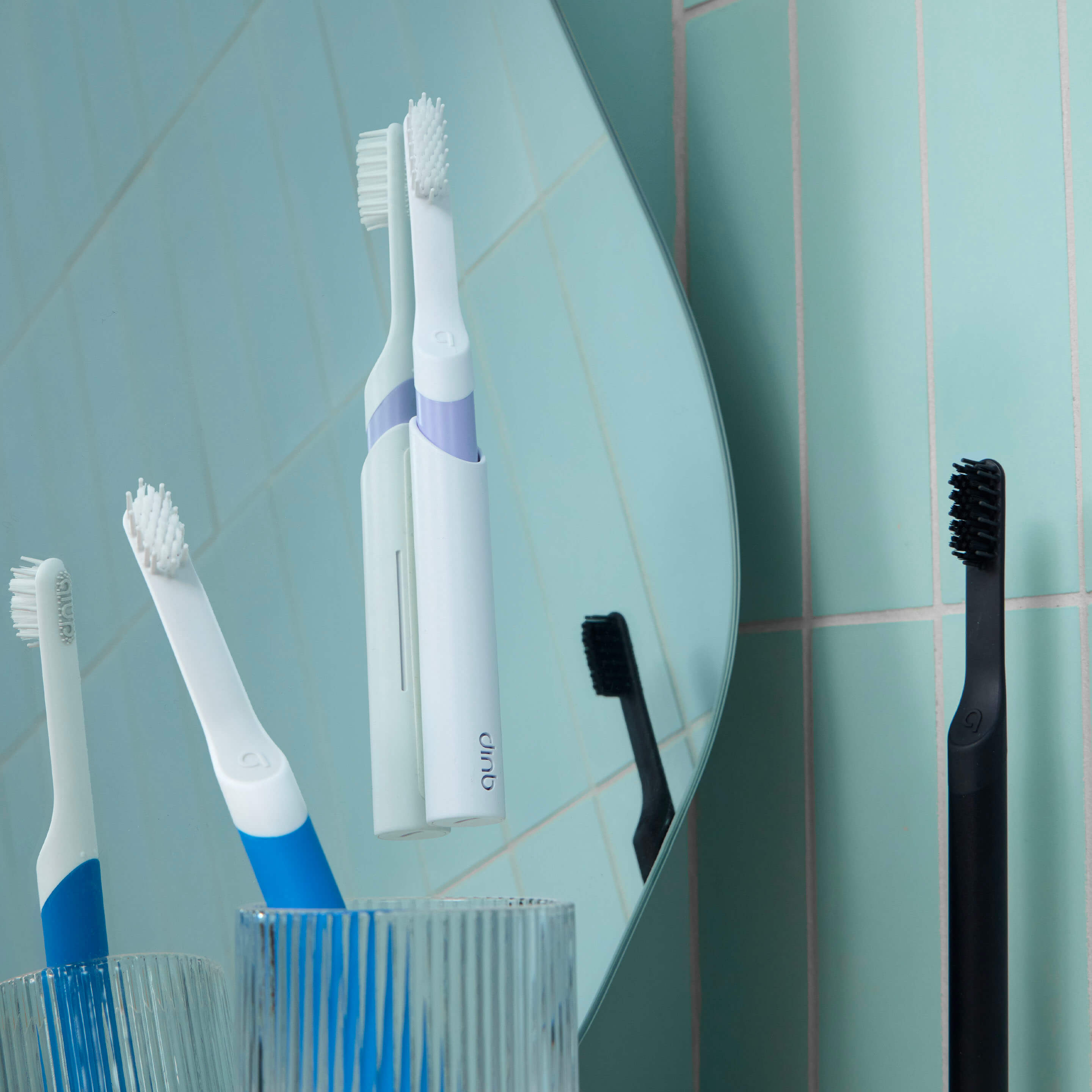 Set of electric toothbrushes with a holder against a tiled bathroom wall.