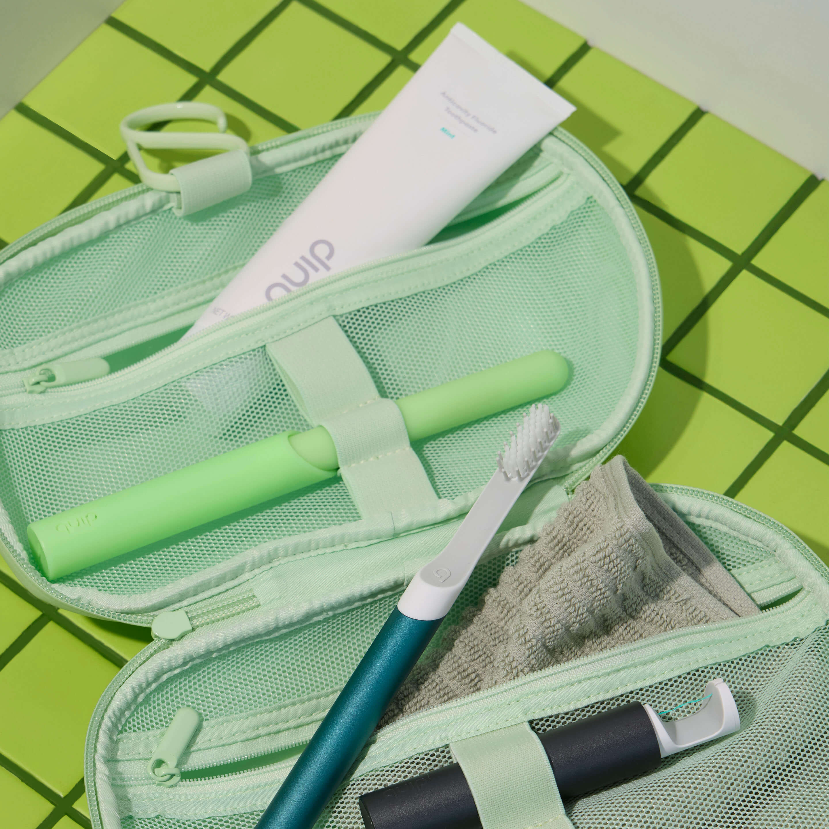 Green travel toiletry bag with toothbrush, toothpaste, and other items on a green grid background