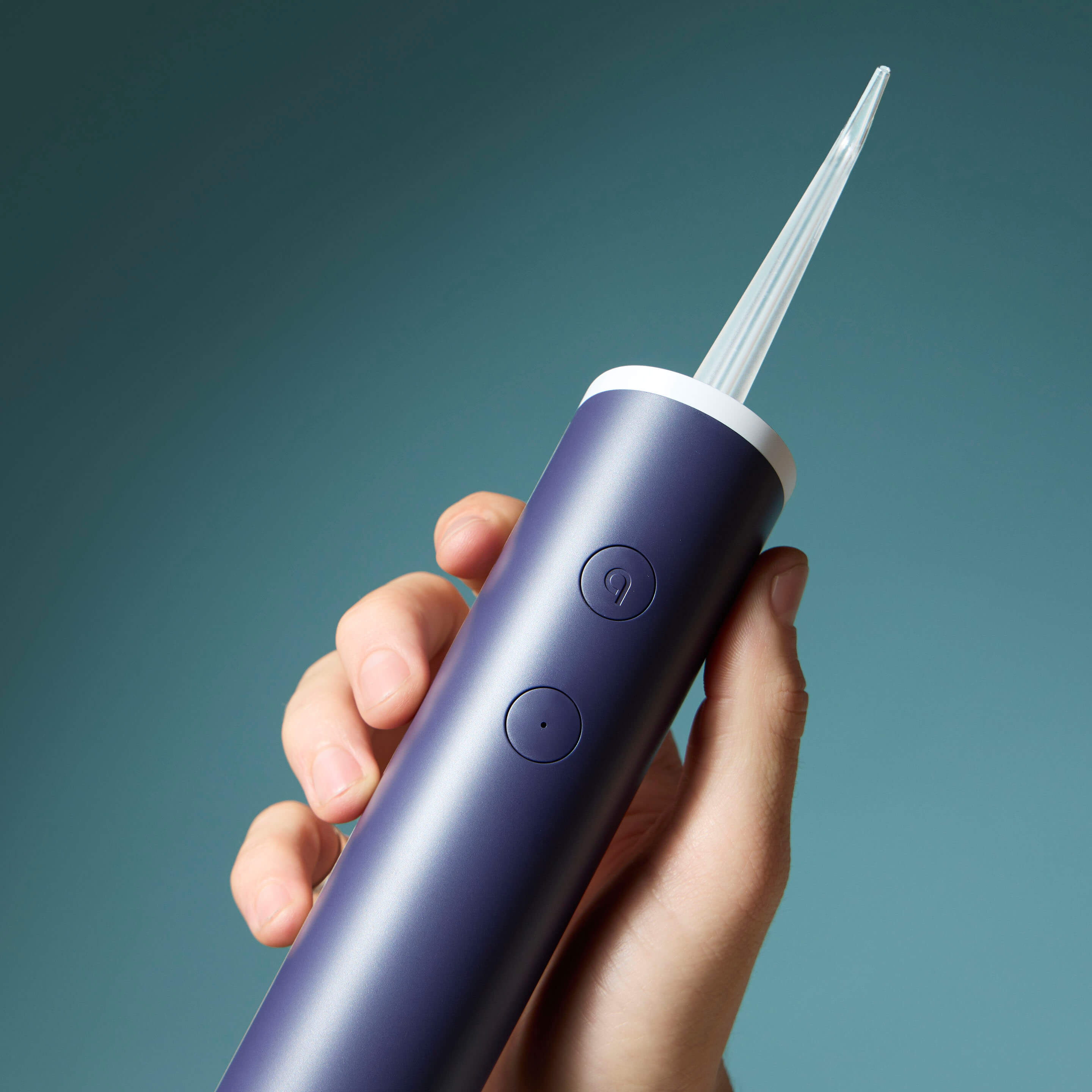 Hand holding a purple dental water flosser against a blue background