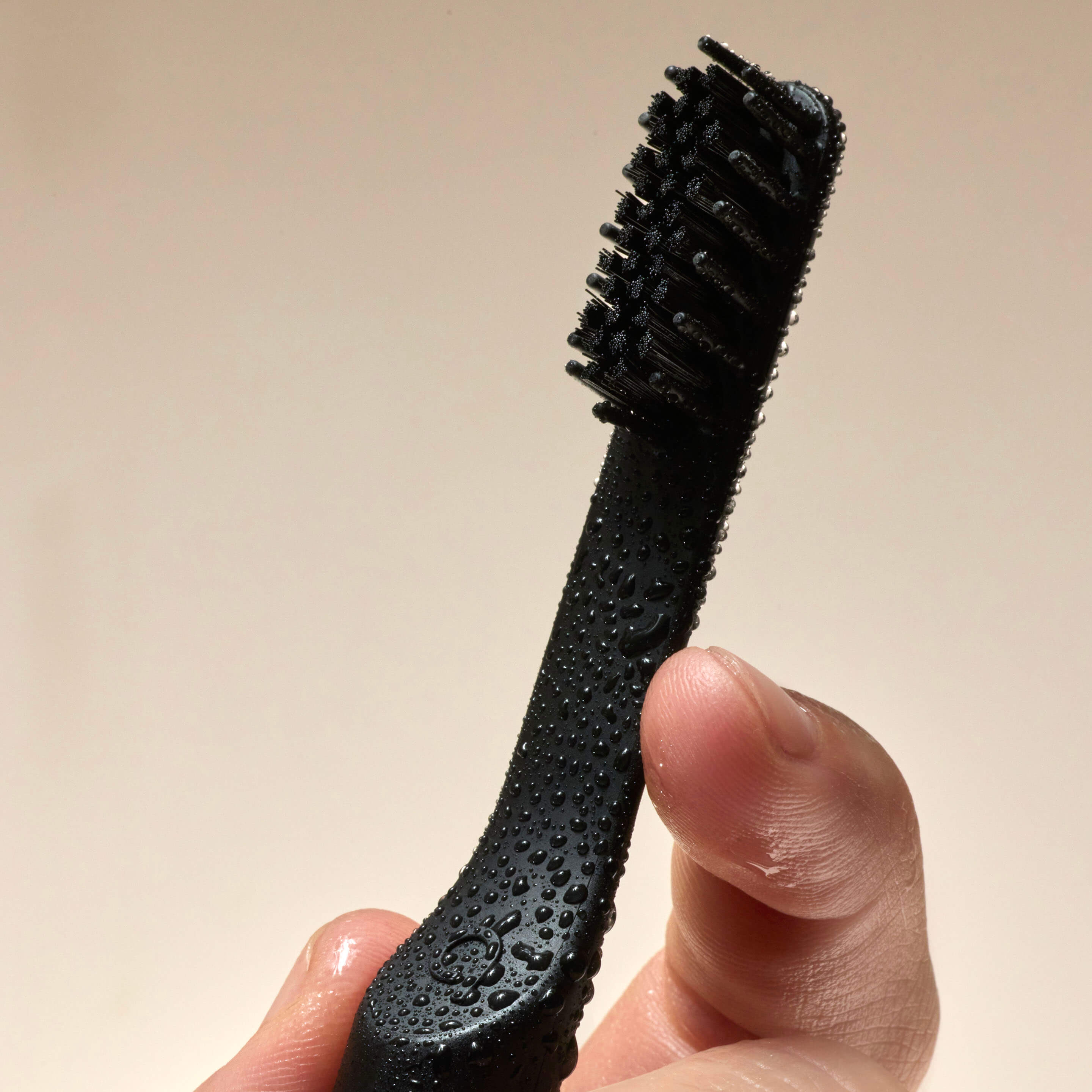 Close-up of a hand holding a black toothbrush head covered in water droplets, against a neutral background.