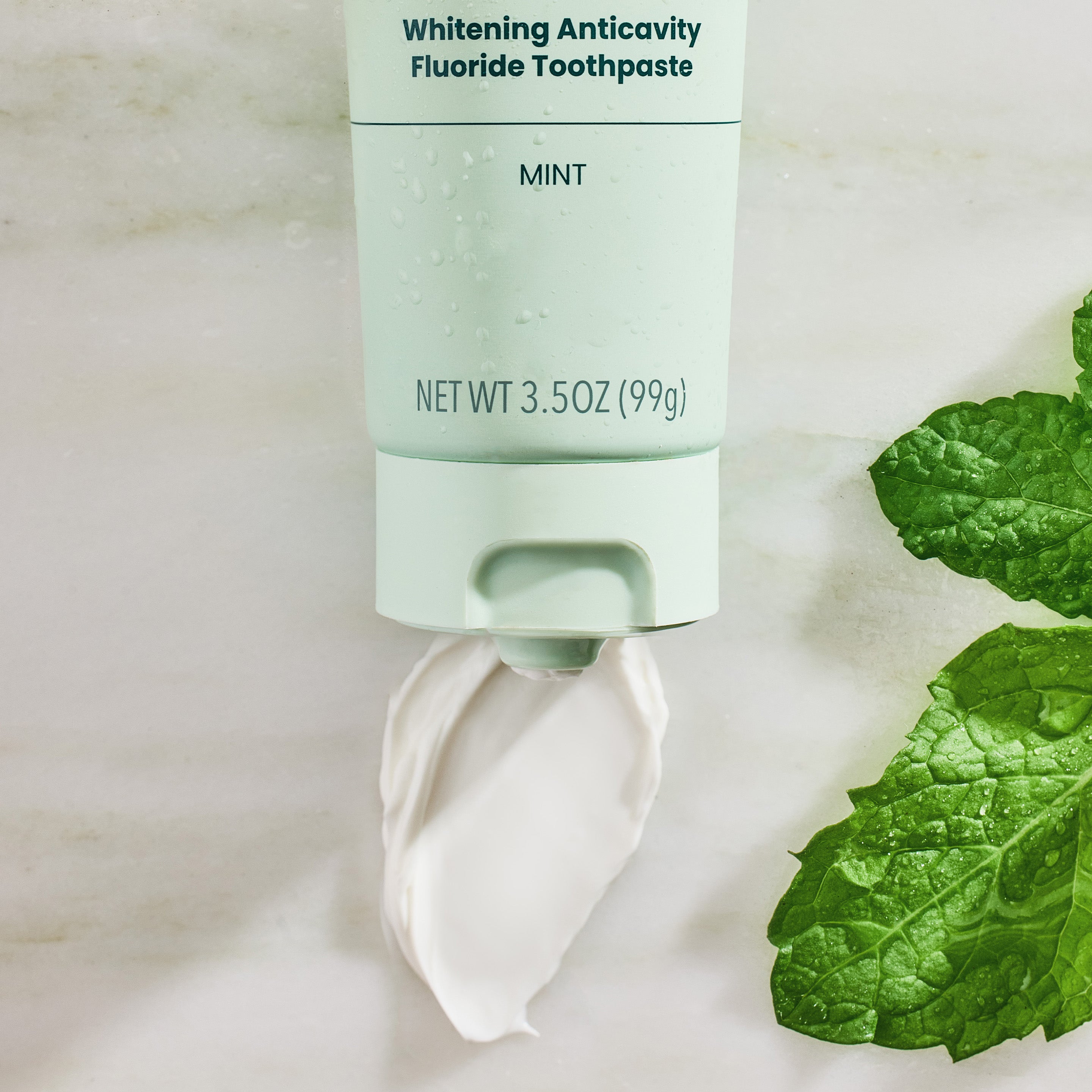 Mint-flavored toothpaste with a smear of toothpaste and mint leaves on a light background