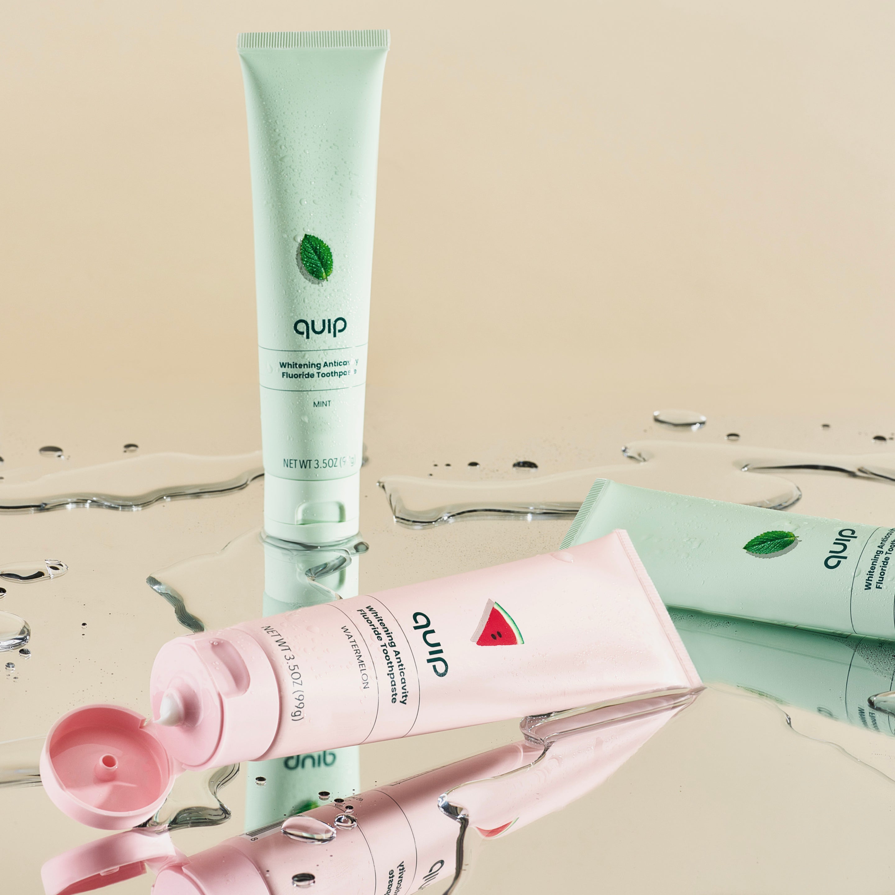 Two toothpaste tubes, one green and one pink, with 'quip' branding on a neutral background.