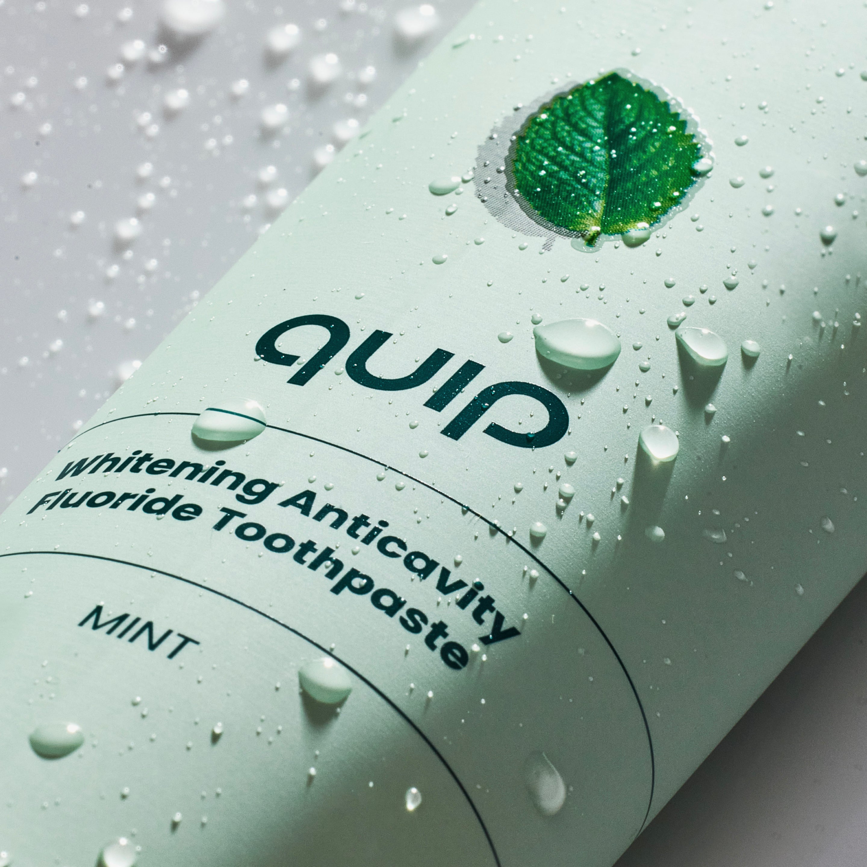 QUIP mint toothpaste tube with water droplets on a light background