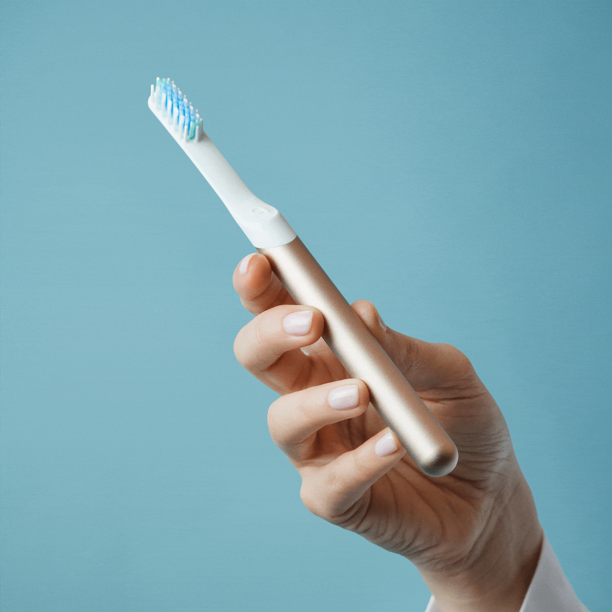Close-up of hands holding an electric toothbrush with the detachable brush head removed, showing the connection point against a blue background.