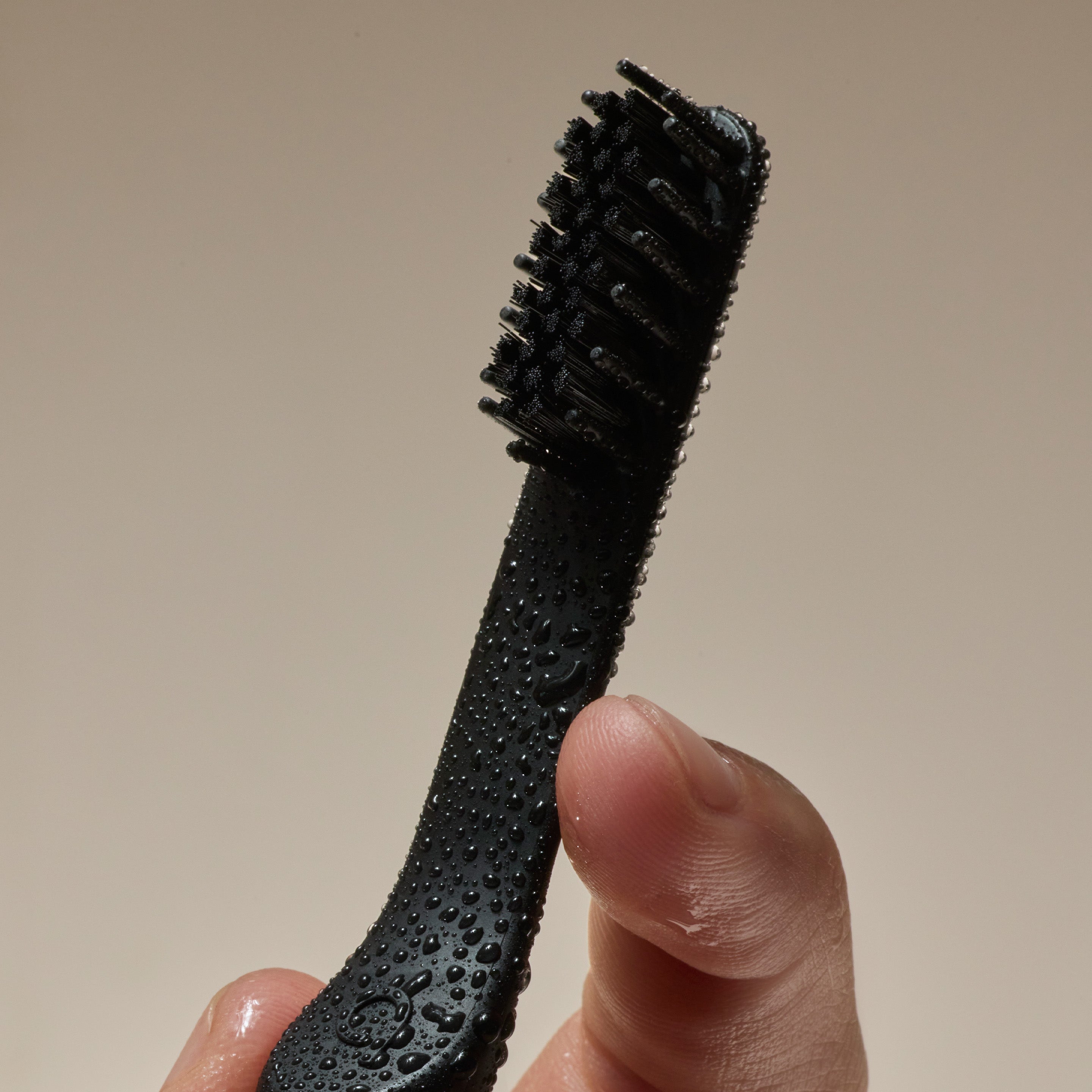 Hand holding a wet black toothbrush with water droplets on the handle and bristles.