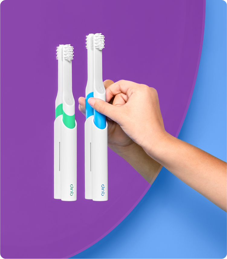 a green and a blue quip kids sonic toothbrush mounted on the bathroom mirror, with a model reaching for the blue brush