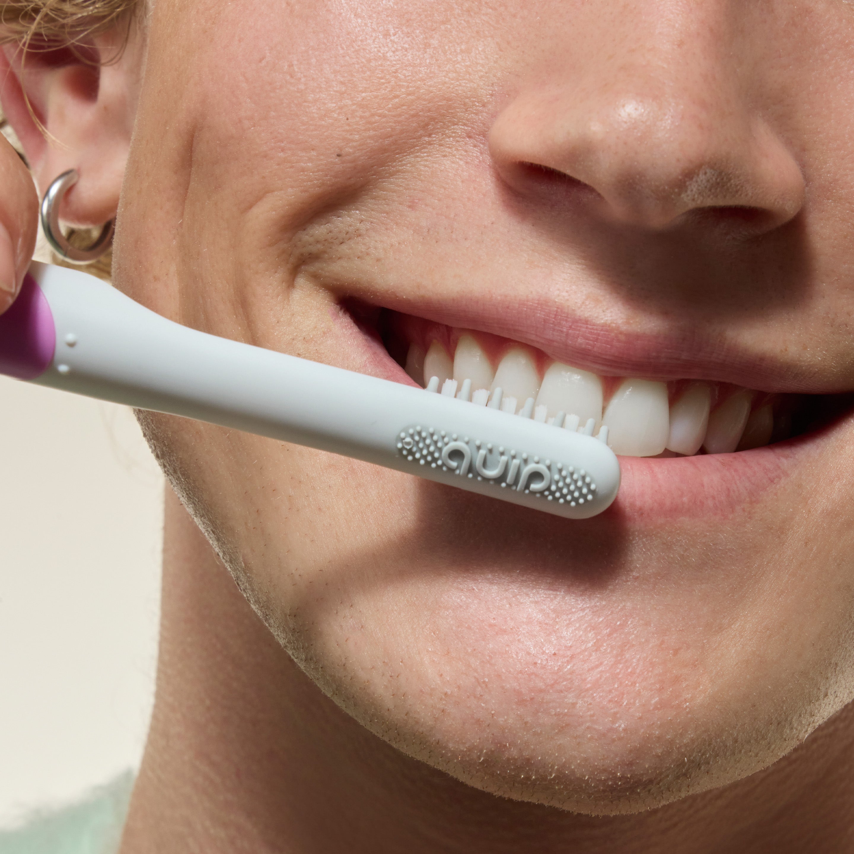 Person smiling while brushing their teeth with a white toothbrush held against their front teeth.