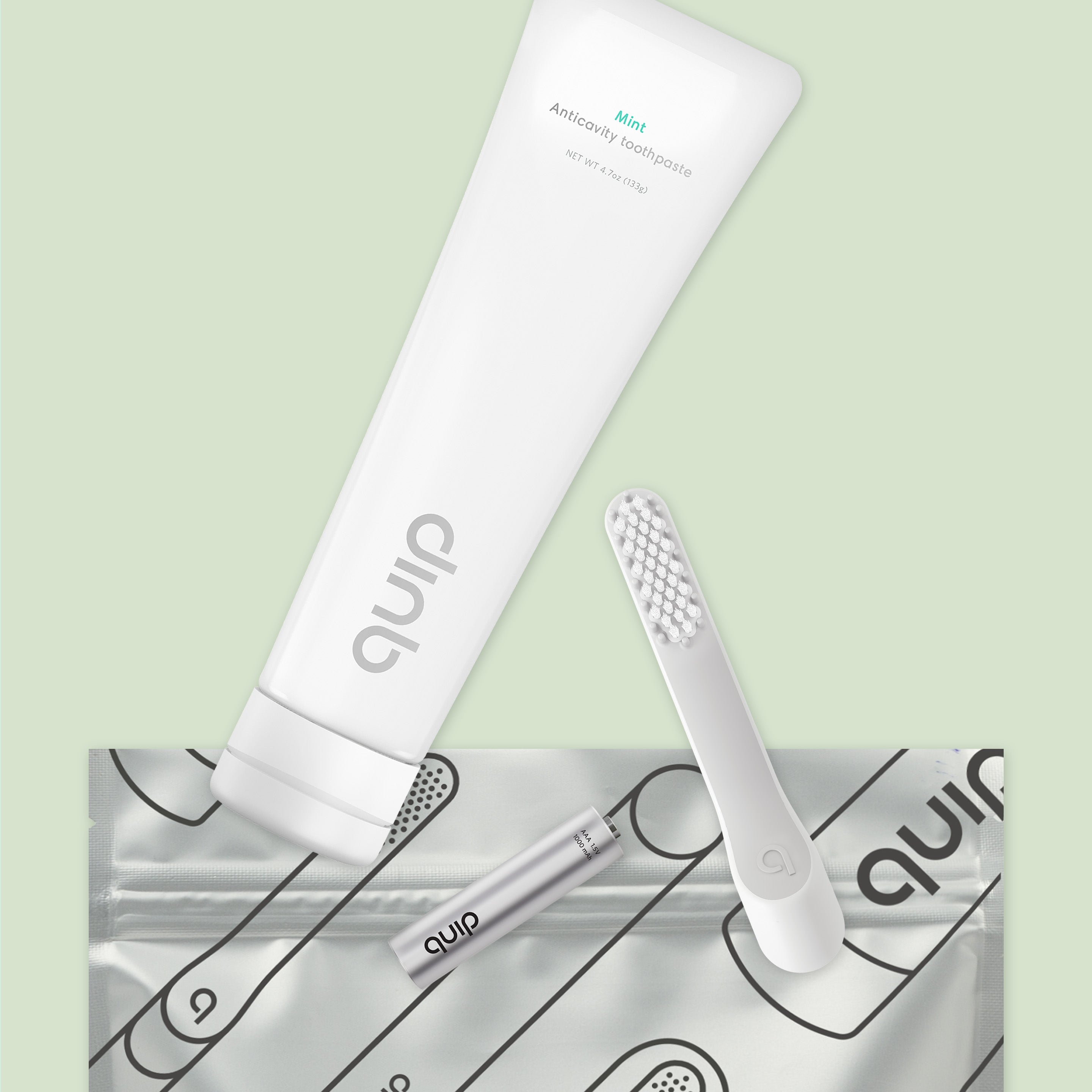 Flat lay of a white toothpaste tube, toothbrush head, battery, and patterned pouch on a light green background.
