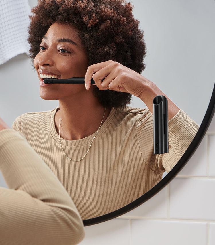 A model smiles while brushing her teeth with quip Sonic Rechargeable Brush