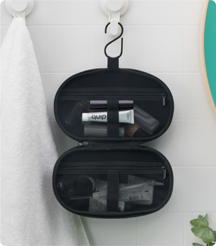 black quip refresh bag is hooked next to the bath towel in the bathroom, featuring storage straps and mesh pockets for organization