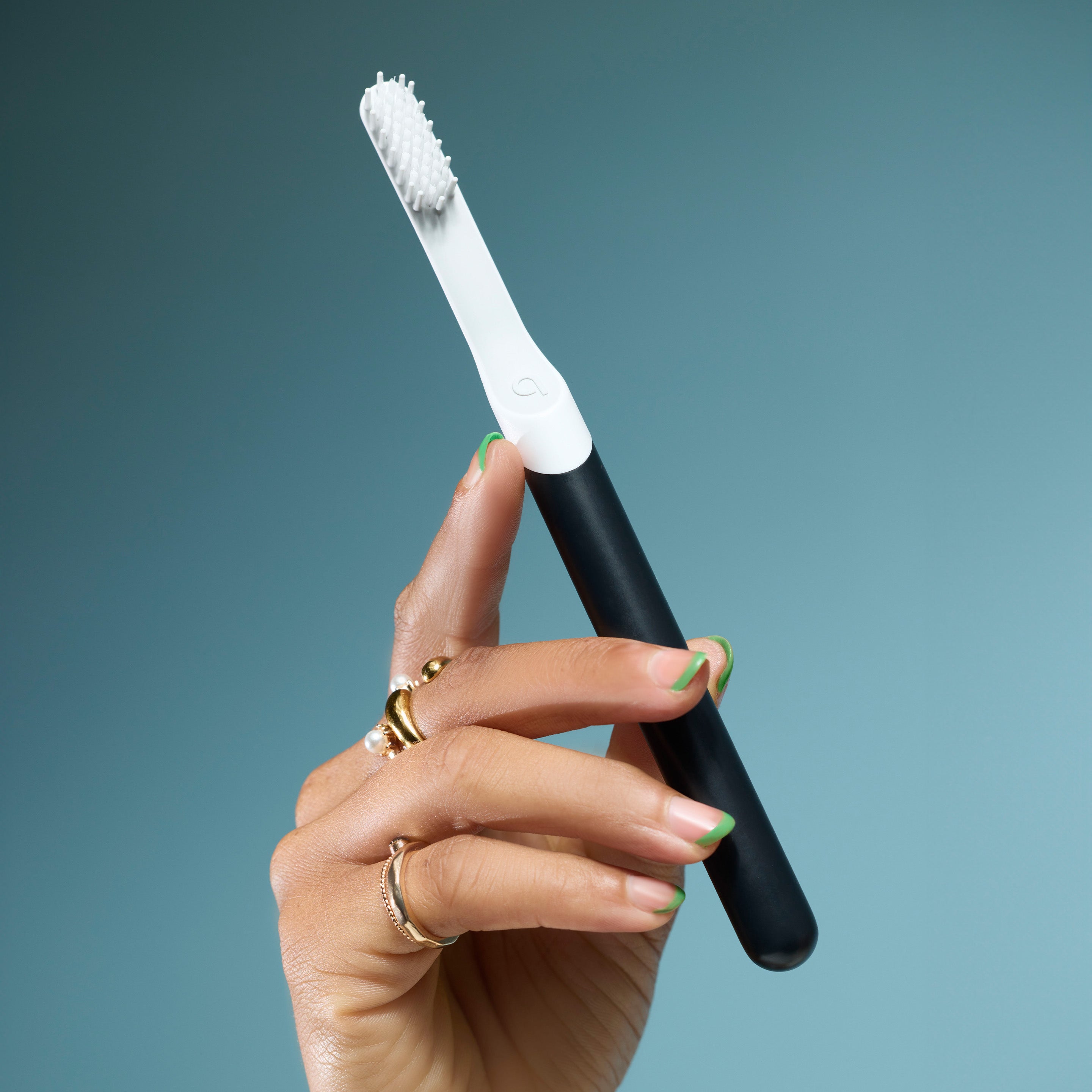 Hand holding a black-and-white toothbrush against a teal background.