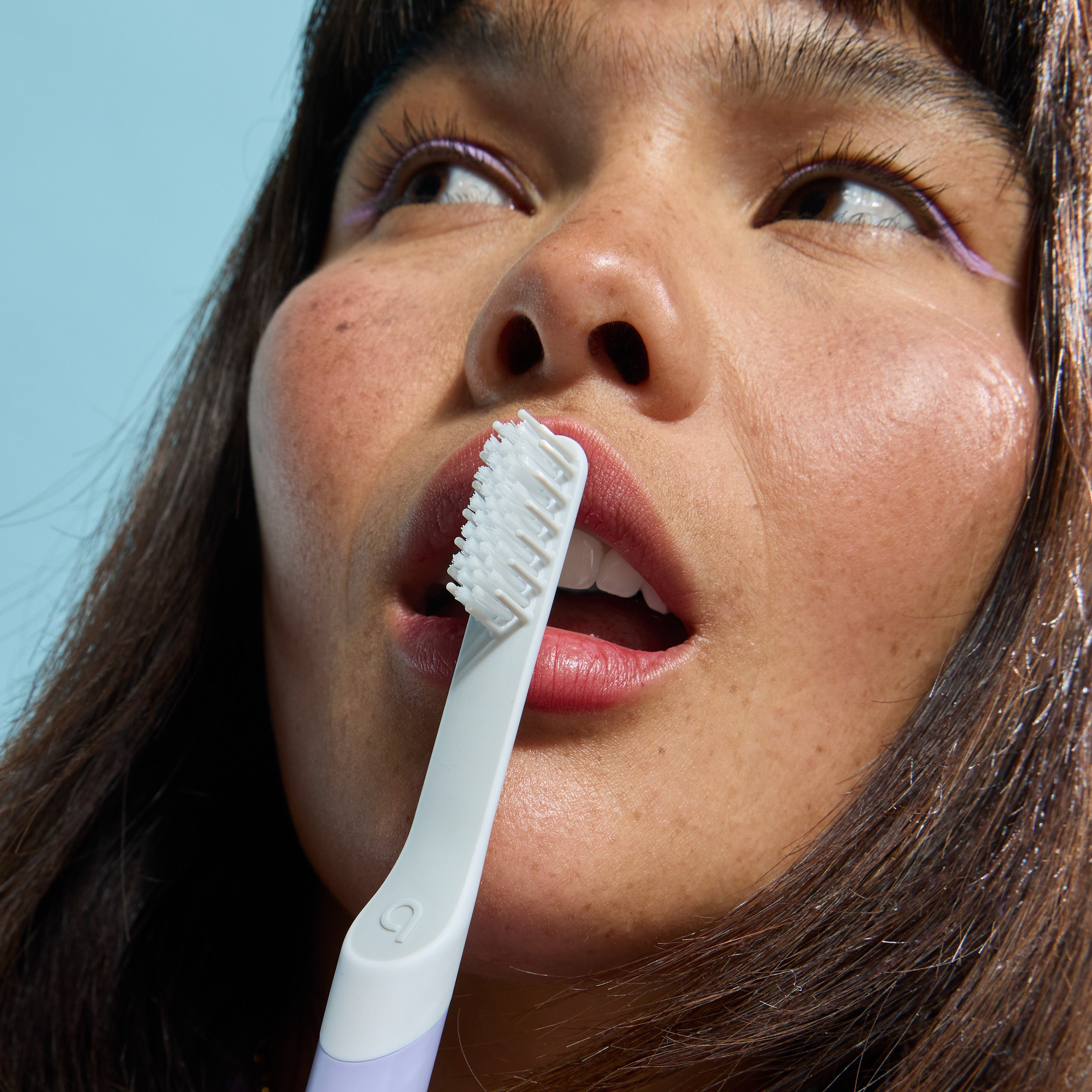 Close-up of a person holding a white toothbrush near their lips against a light blue background.