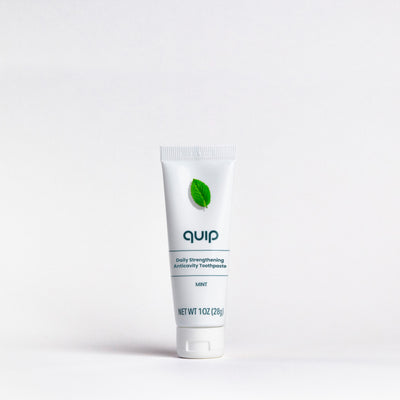 A white squeeze tube of quip Daily Strengthening Anticavity Toothpaste in Mint flavor, featuring a green leaf logo, centered on a clean white background.