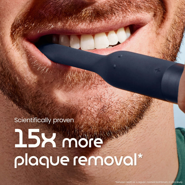 Close-up of a person using a black electric toothbrush with text about plaque removal.