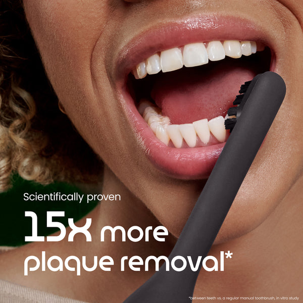 Close-up of a person brushing their teeth with a black toothbrush, emphasizing plaque removal benefits.