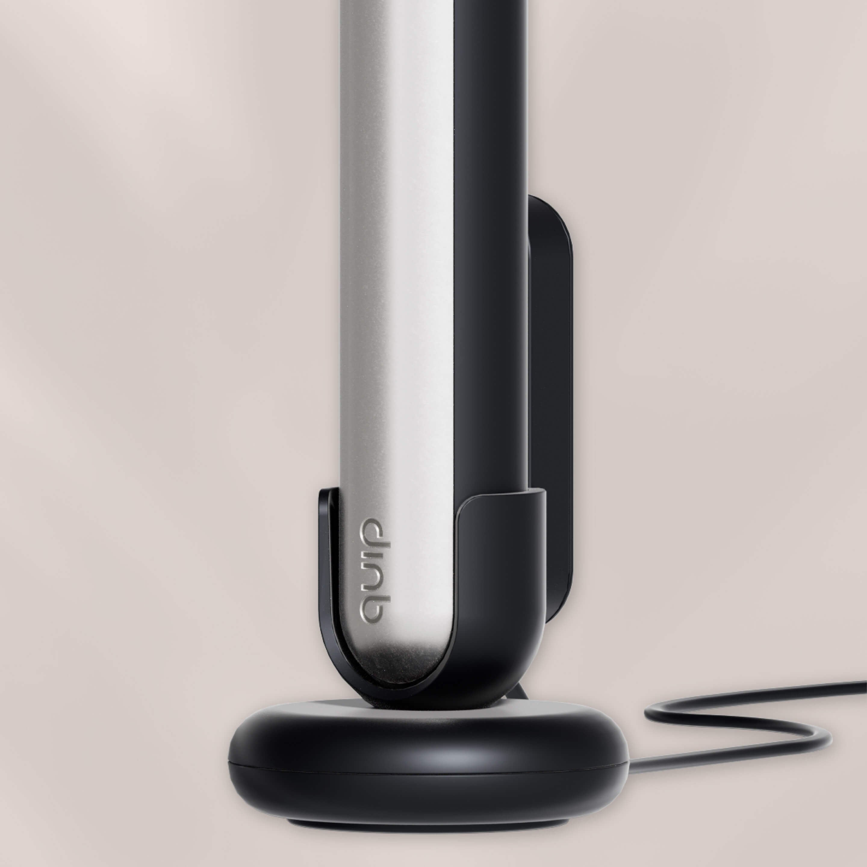 Close-up of a Rev toothbrush standing upright on a black charging base, with the power cable extending to the side.