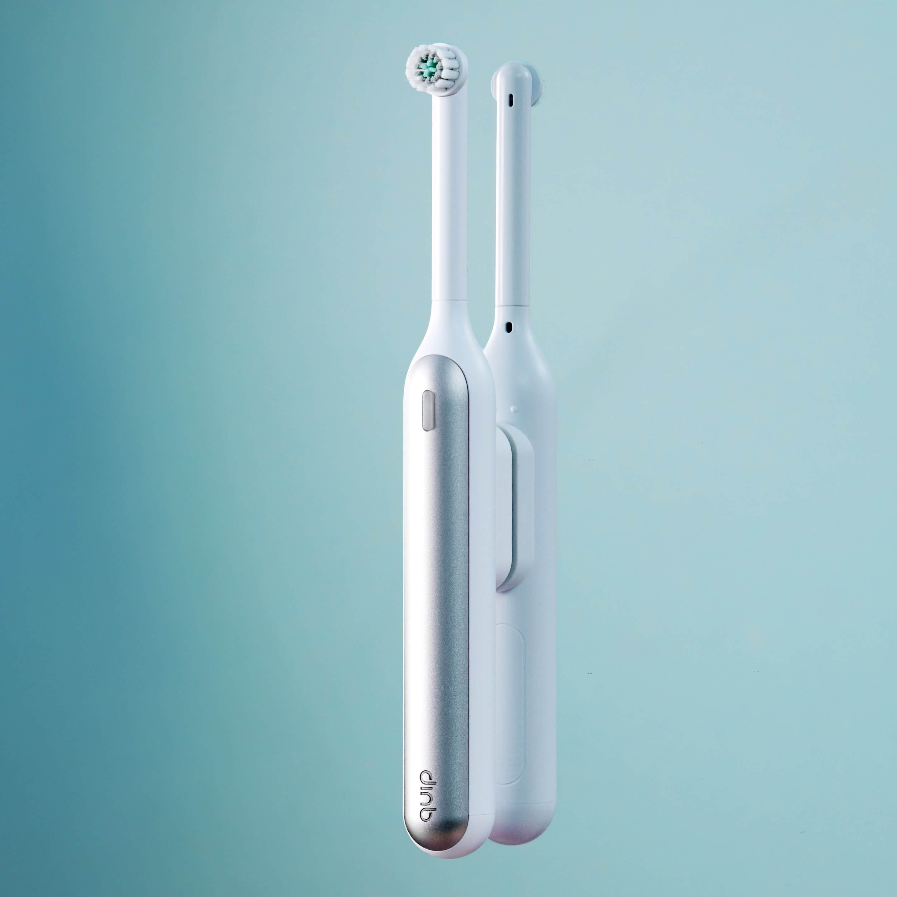 Two quip Rev Oscillating Electric toothbrushes are displayed on a light blue background. The one in the foreground is silver and white, and the one behind it is all white.
