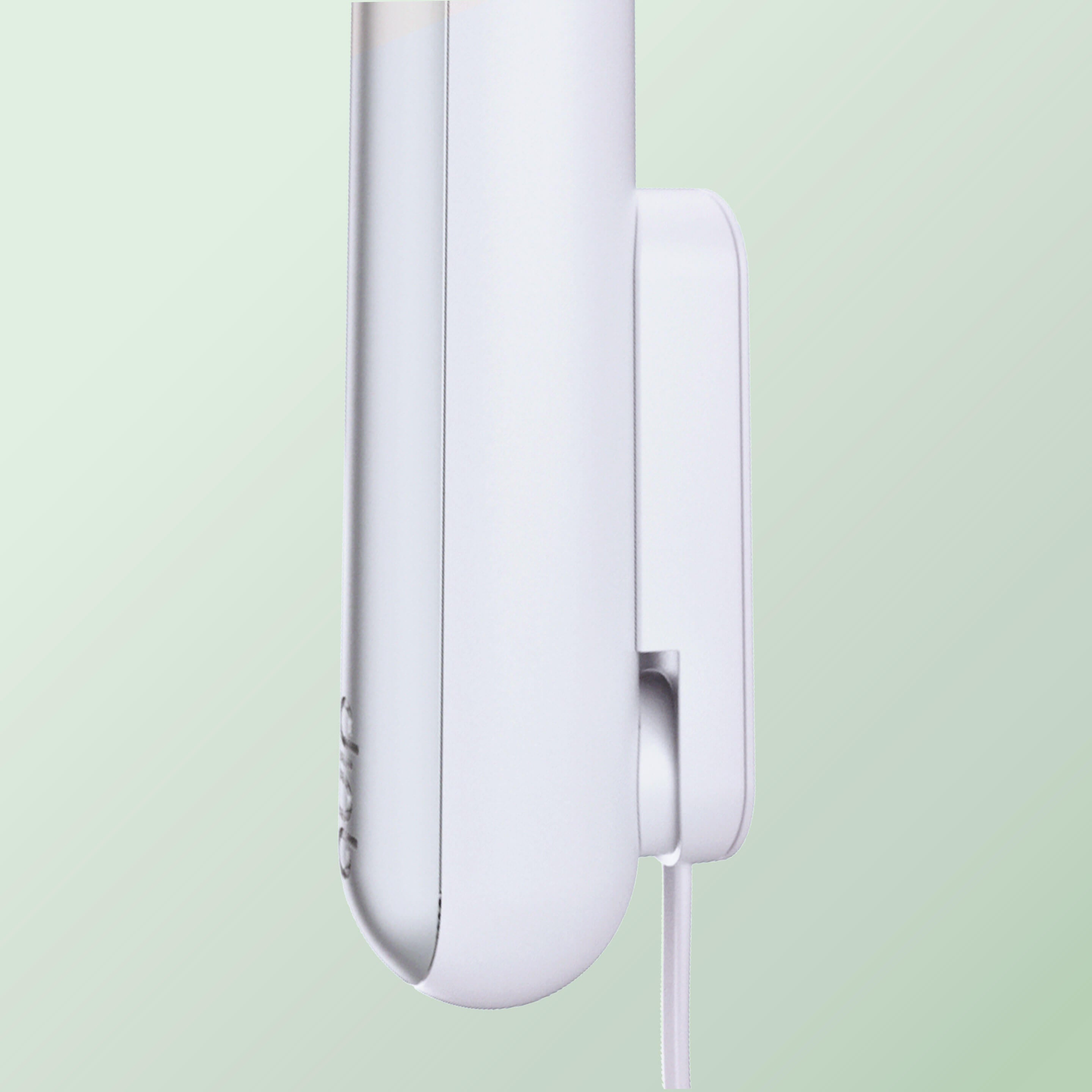Close-up of a white Rev toothbrush resting on a white wall-mounted charger, with the charging cable extending downward against a soft green background.