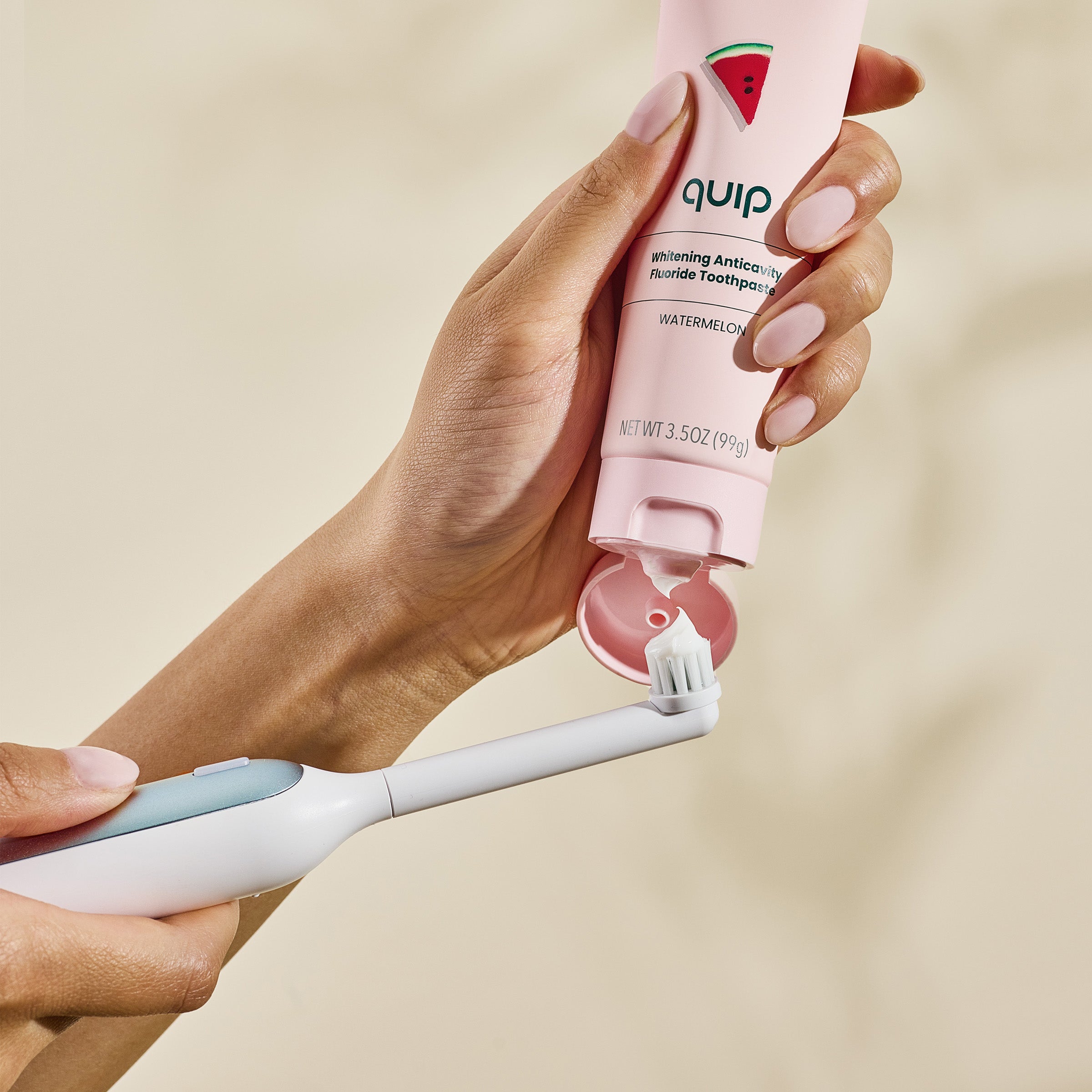 Hand holding a pink 'quip' toothbrush and toothpaste tube on a beige background