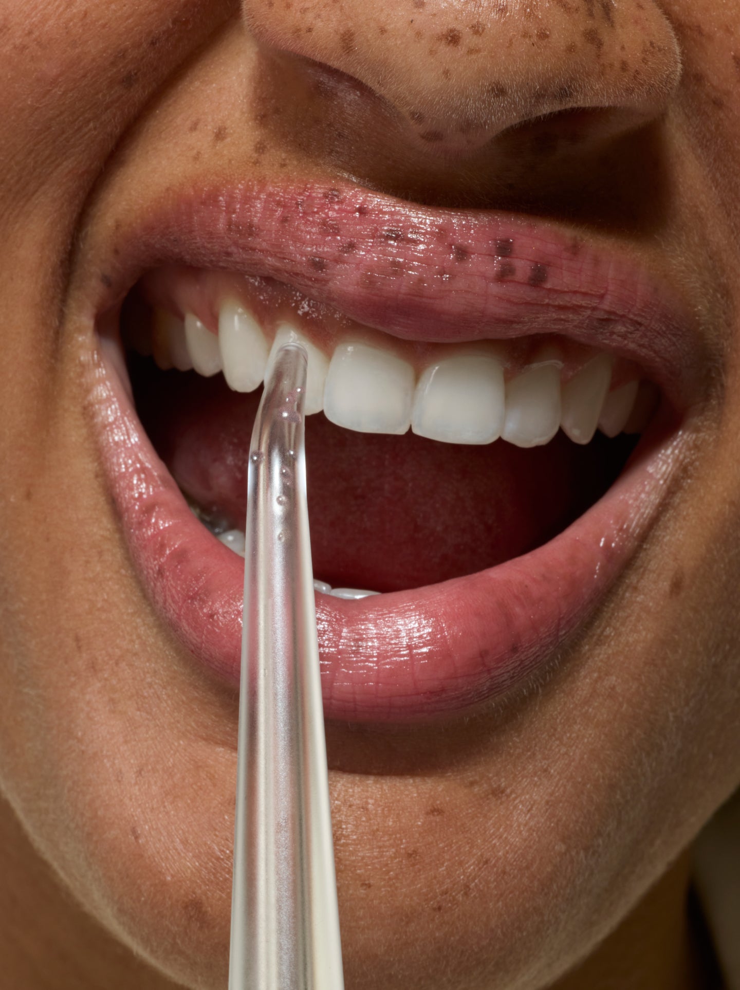Close-up of a person using a water flosser to clean between their teeth, showing healthy gums and glossy lips.