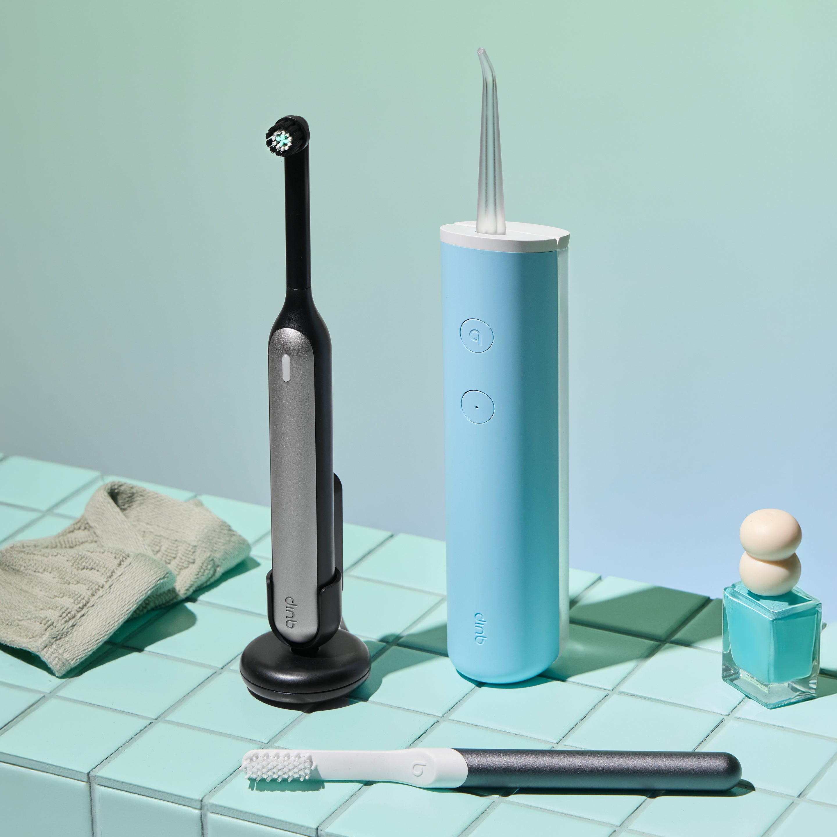 Rev Oscillating Toothbrush in Gray Shadow displayed with a blue water flosser and manual toothbrush on a mint-tiled surface.