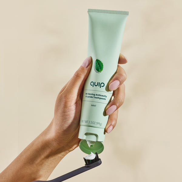 Hand holding a tube of quip toothpaste against a beige background