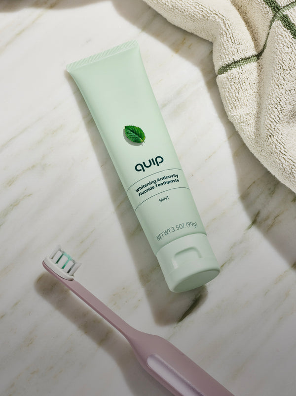 quip Whitening Anticavity Fluoride Toothpaste and quip Ultra Smart Sonic Toothbrush on marble countertop, showcasing premium whitening and oral care essentials.