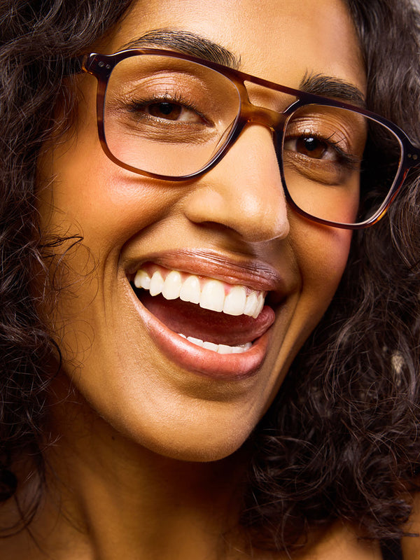 Woman with radiant smile and white teeth wearing brown tortoiseshell glasses, showcasing healthy teeth and natural beauty.
