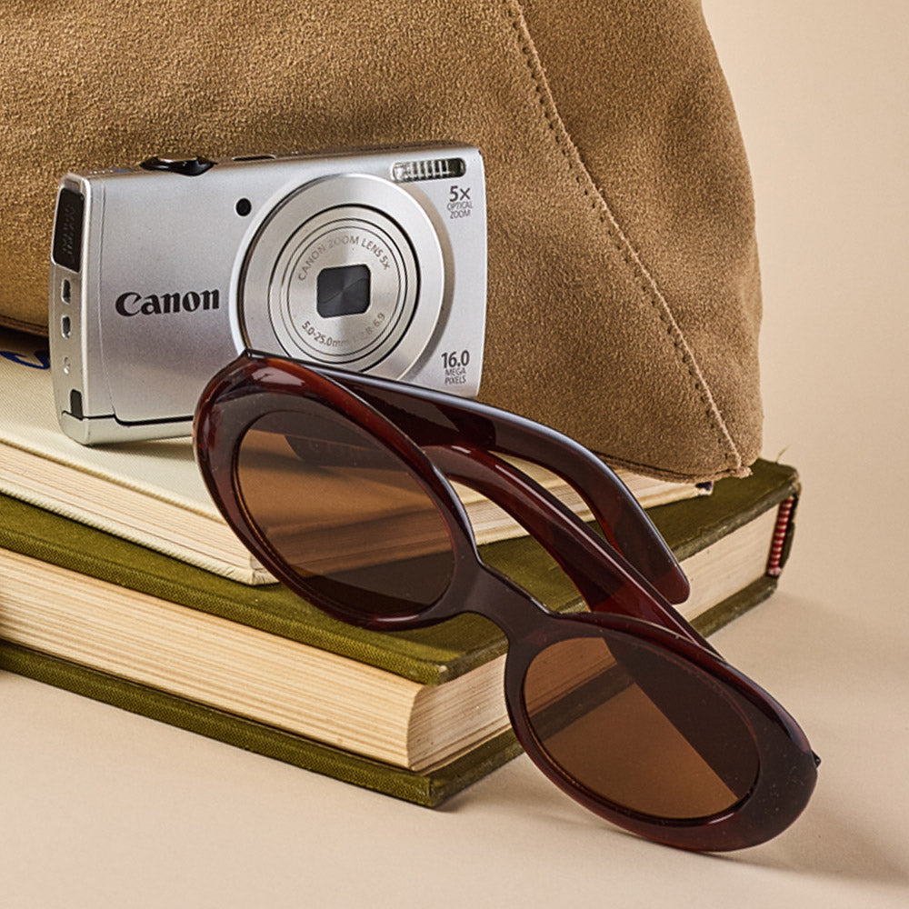 Canon camera on books with sunglasses in front, against a beige background